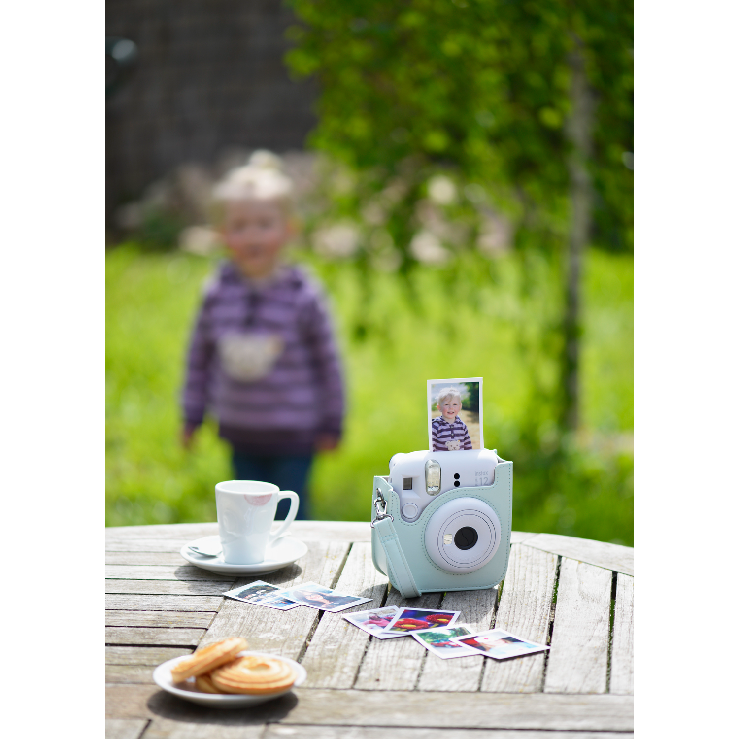 Appareil photo vert menthe, photos sur la table, arrière-plan flou avec fille, tasse, biscuits.