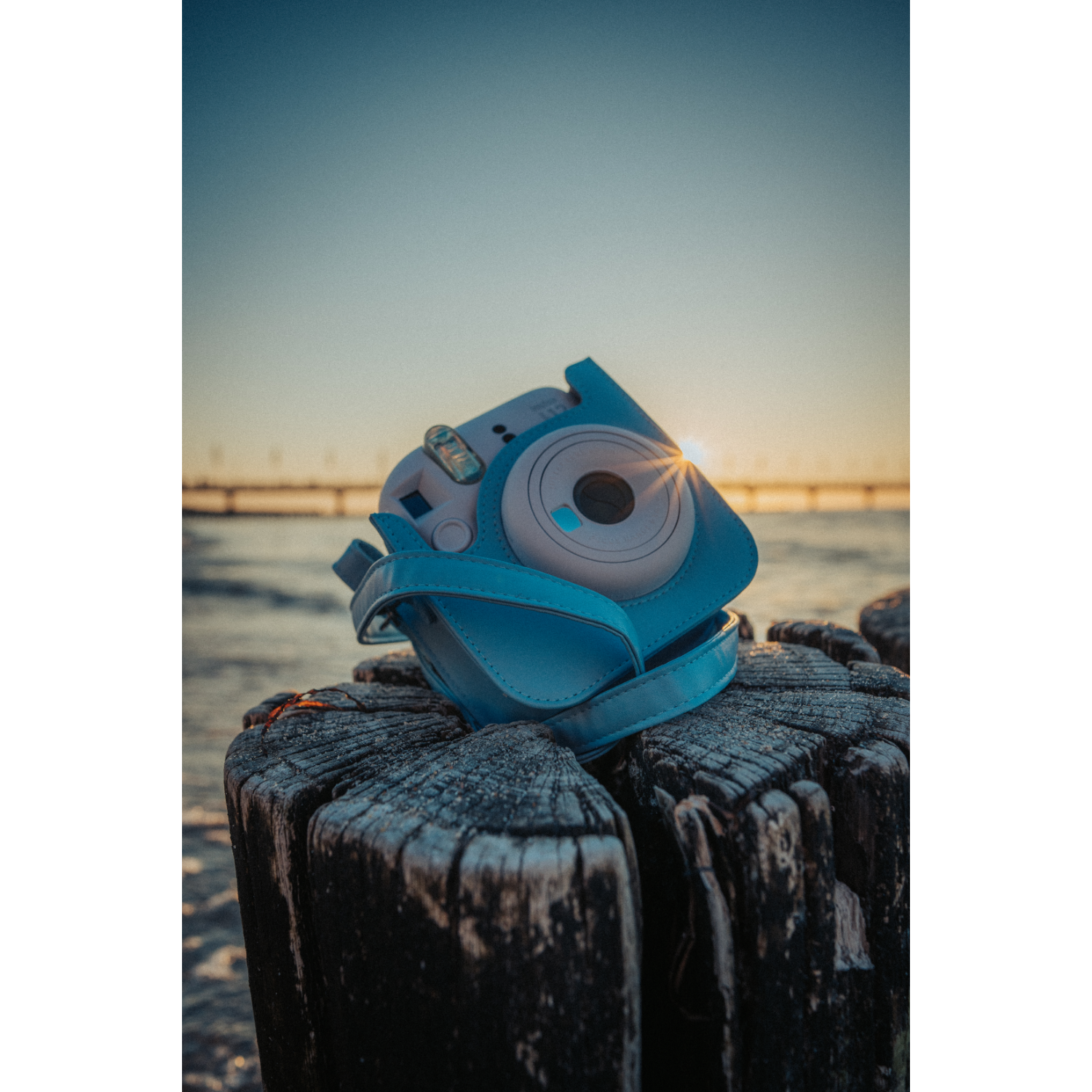 Blaue Kamera in einer Hülle auf einem Holzpfosten mit Sonnenuntergang im Hintergrund.