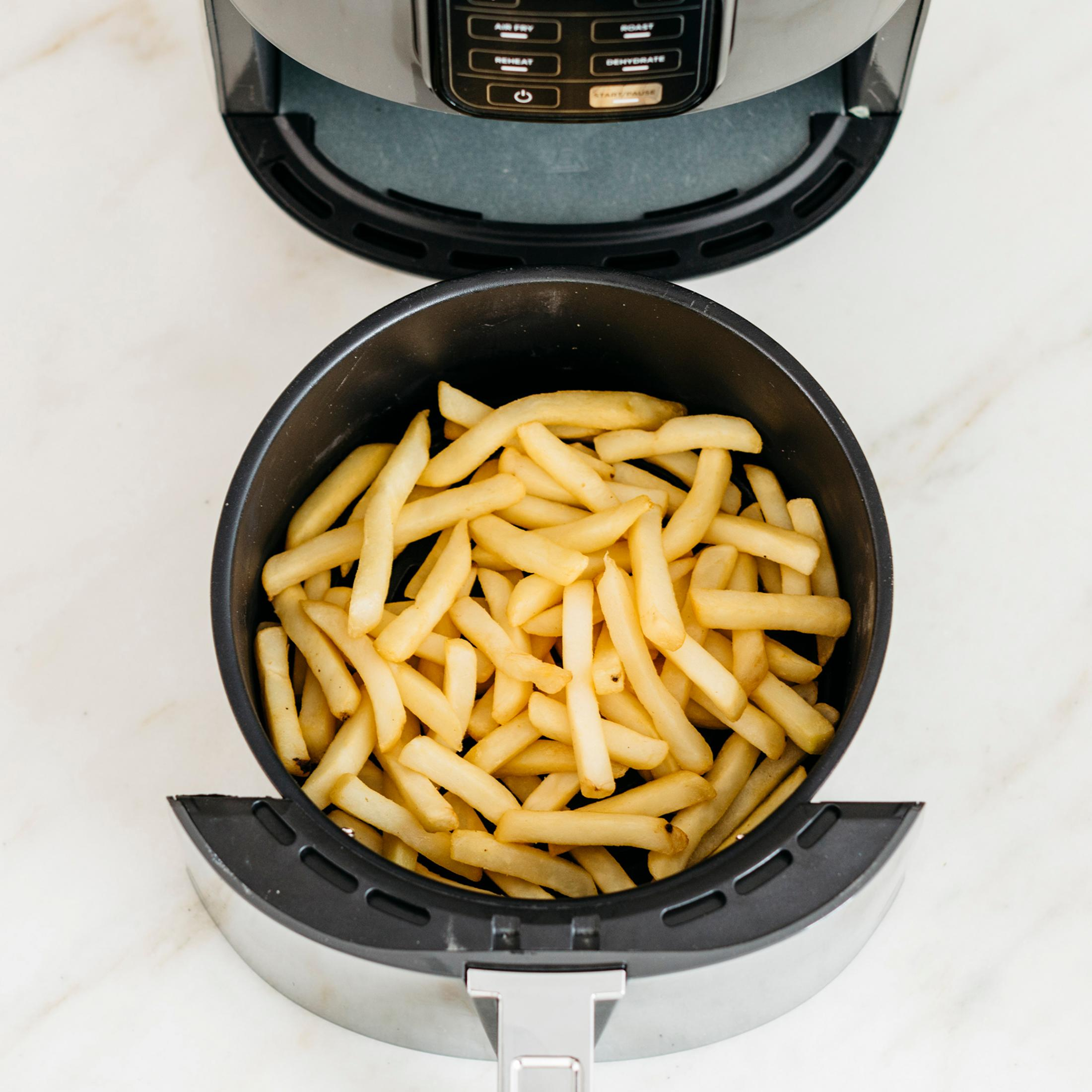 Kosz frytownicy powietrznej wypełniony złotymi frytkami, na białej marmurowej powierzchni.