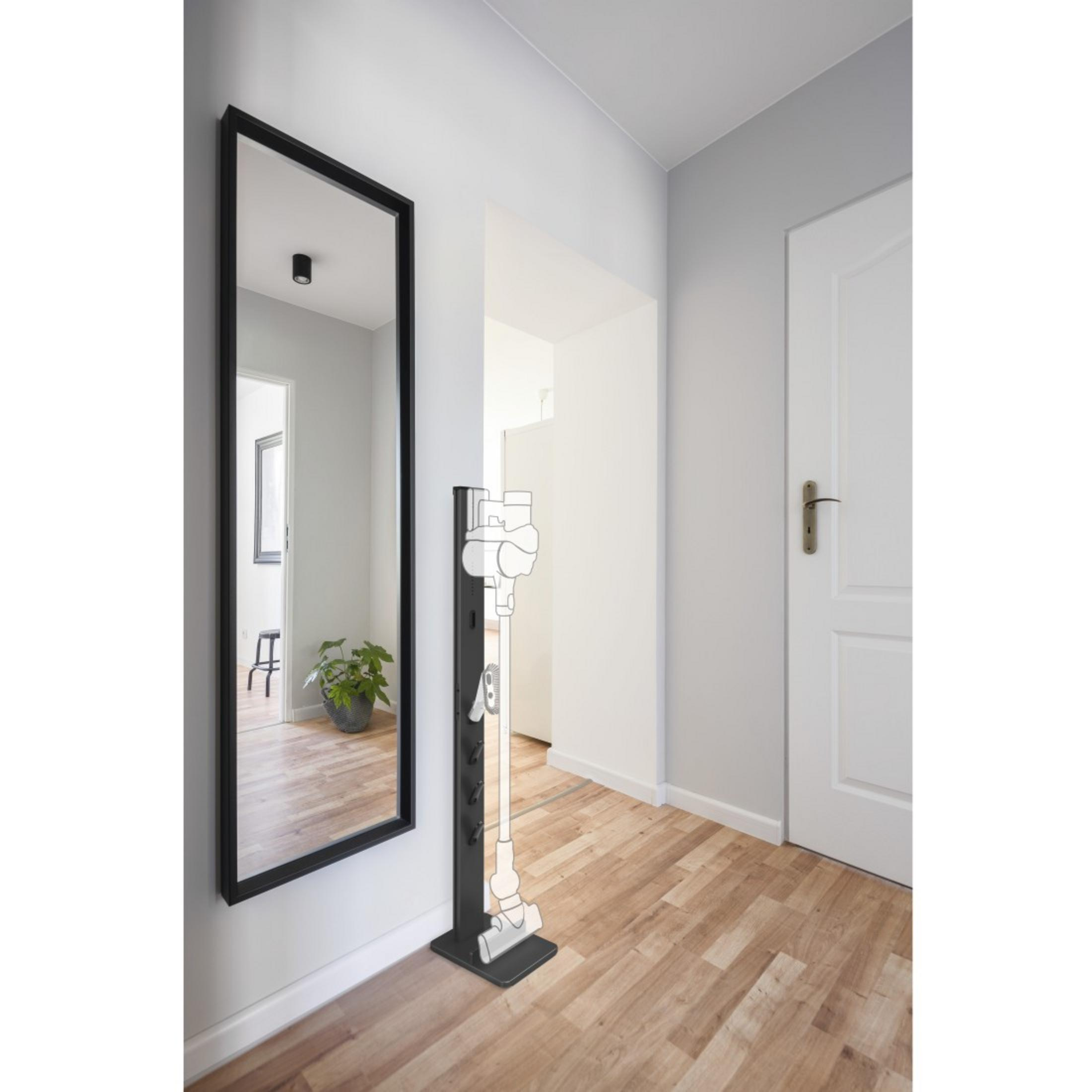 Un pasillo con un gran espejo y un soporte para aspiradora, que refleja la habitación.