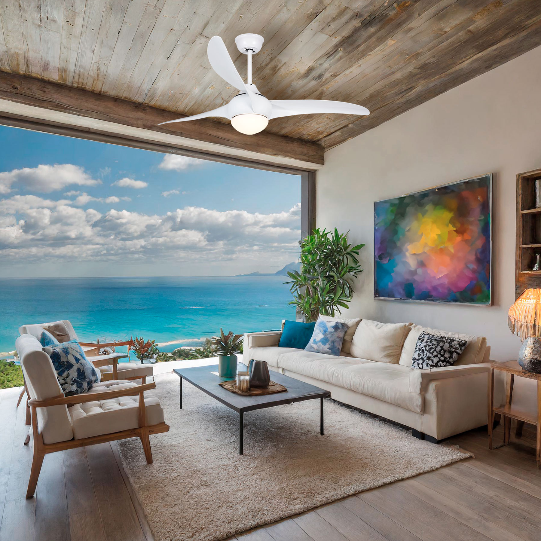 Salón con ventilador de techo, sofá, sillas, obras de arte y una gran ventana con vistas al mar.