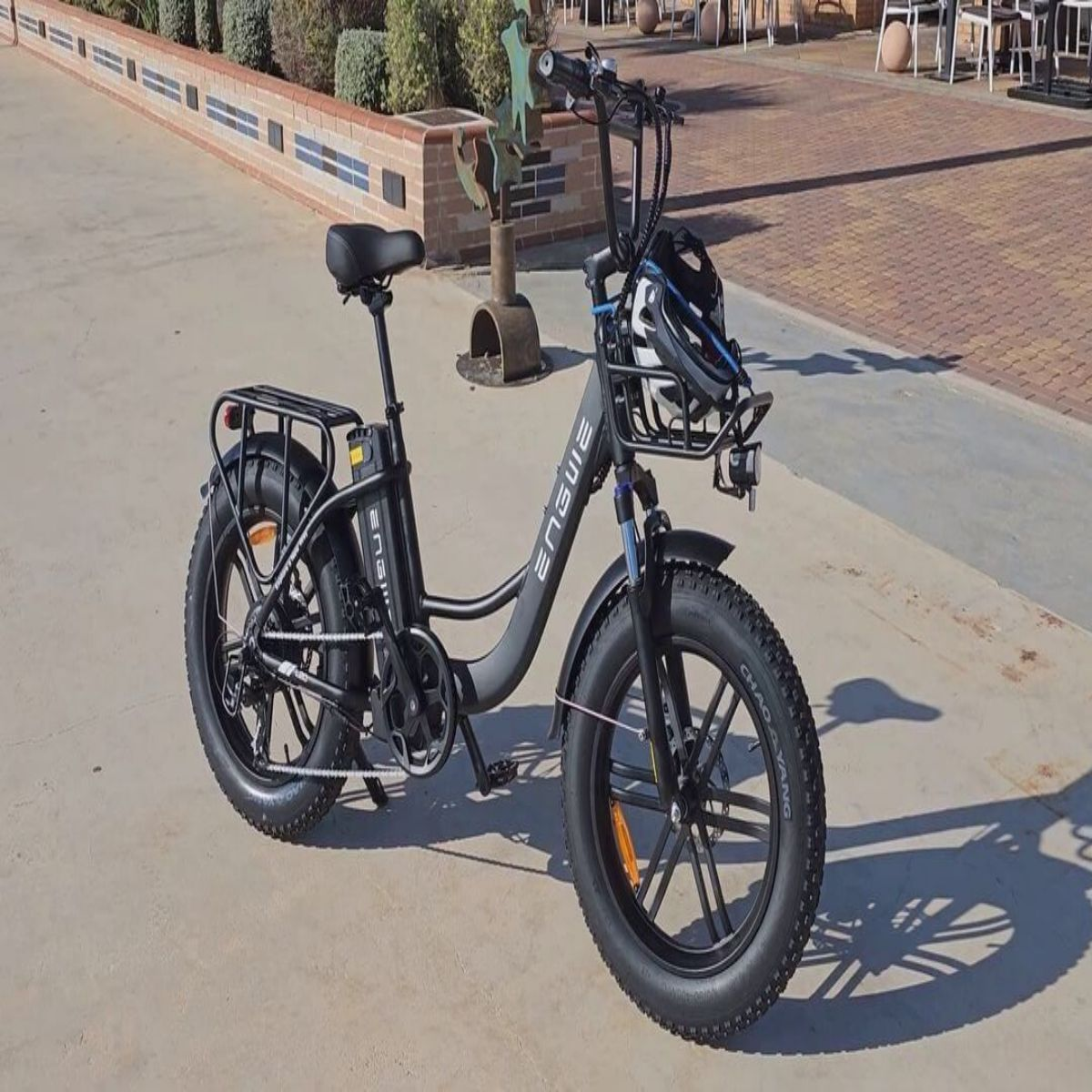 Bicicletta elettrica nera sull'asfalto. Ha un cestino, un sedile e un casco. Sfondo di un edificio.