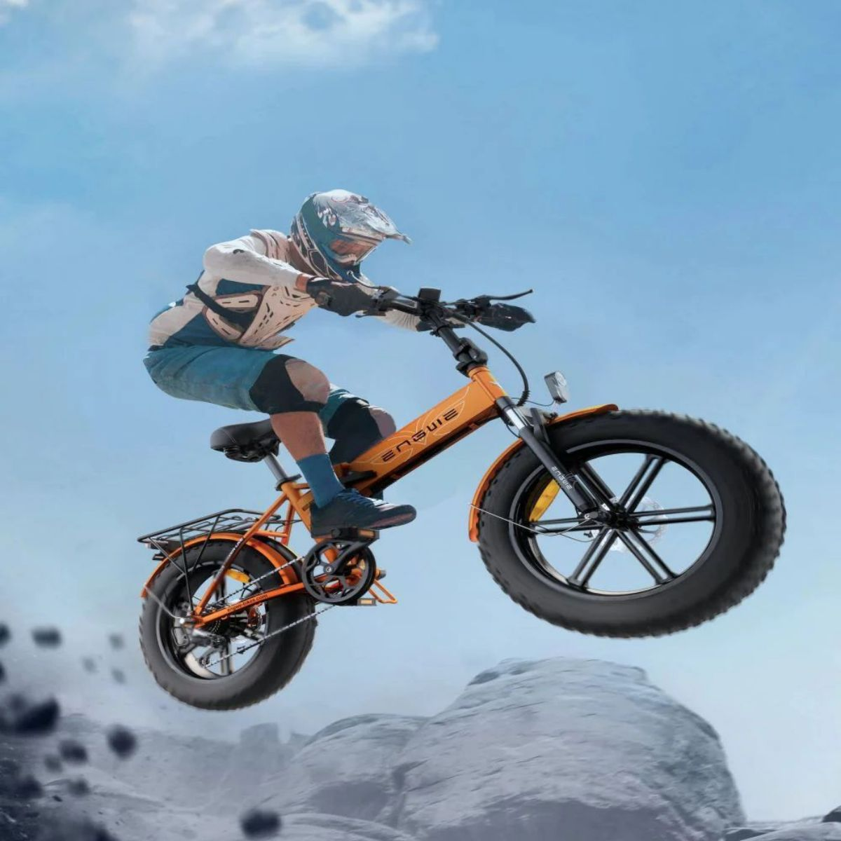 Una persona su una mountain bike arancione salta sopra una collina. Il cielo è blu.