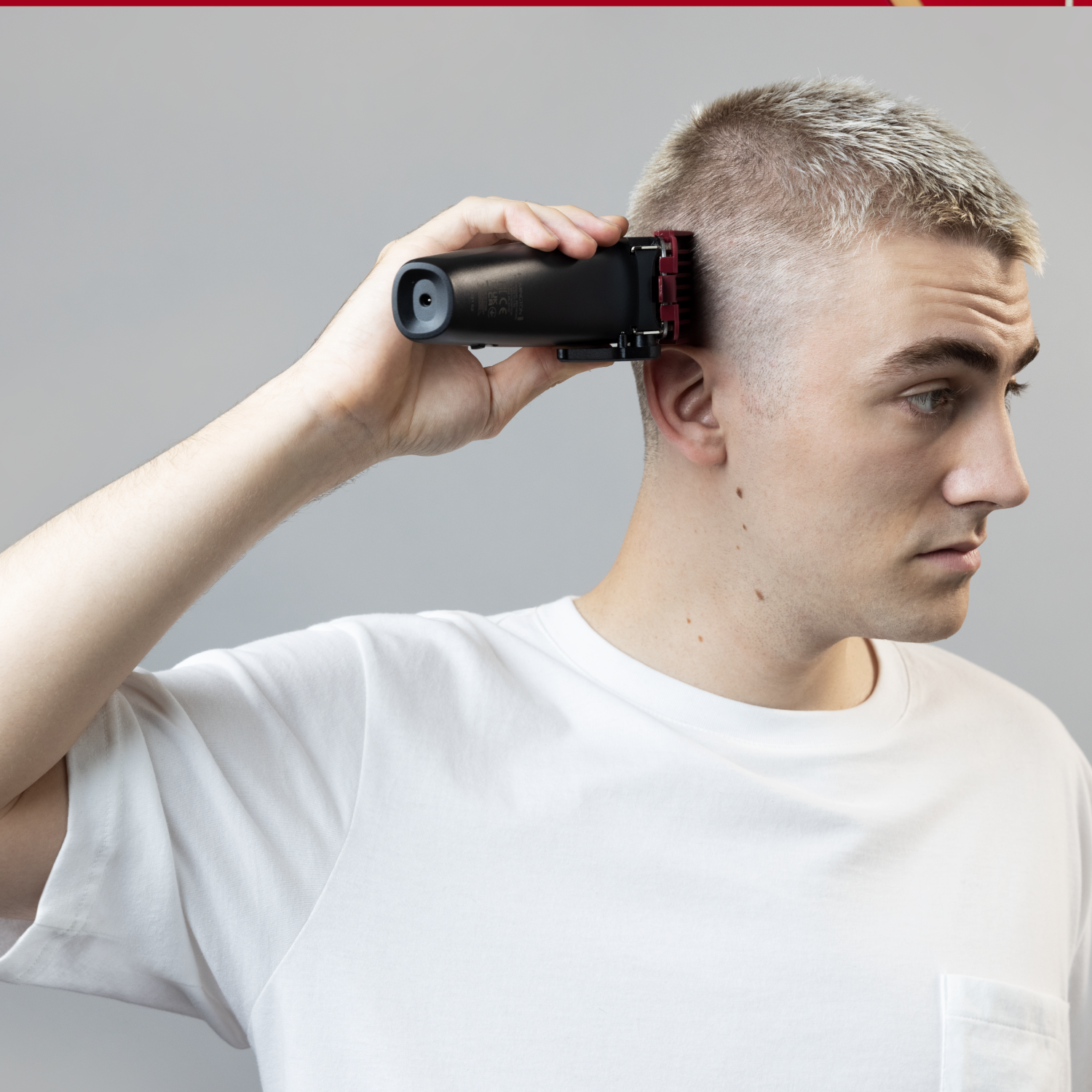 Ein Mann rasiert sich mit einem schwarzen Haarschneider den Kopf und trägt ein weißes Hemd.
