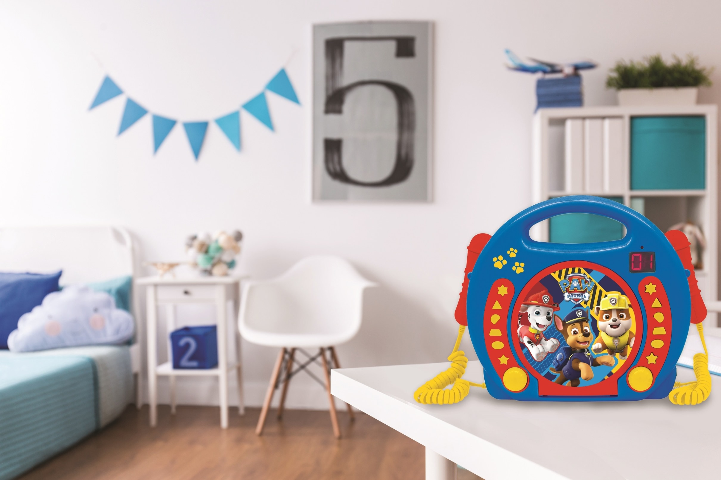 Zabawka odtwarzacza muzyki Paw Patrol na białym stole. Scena przedstawia pokój dziecięcy ze znakiem 5.