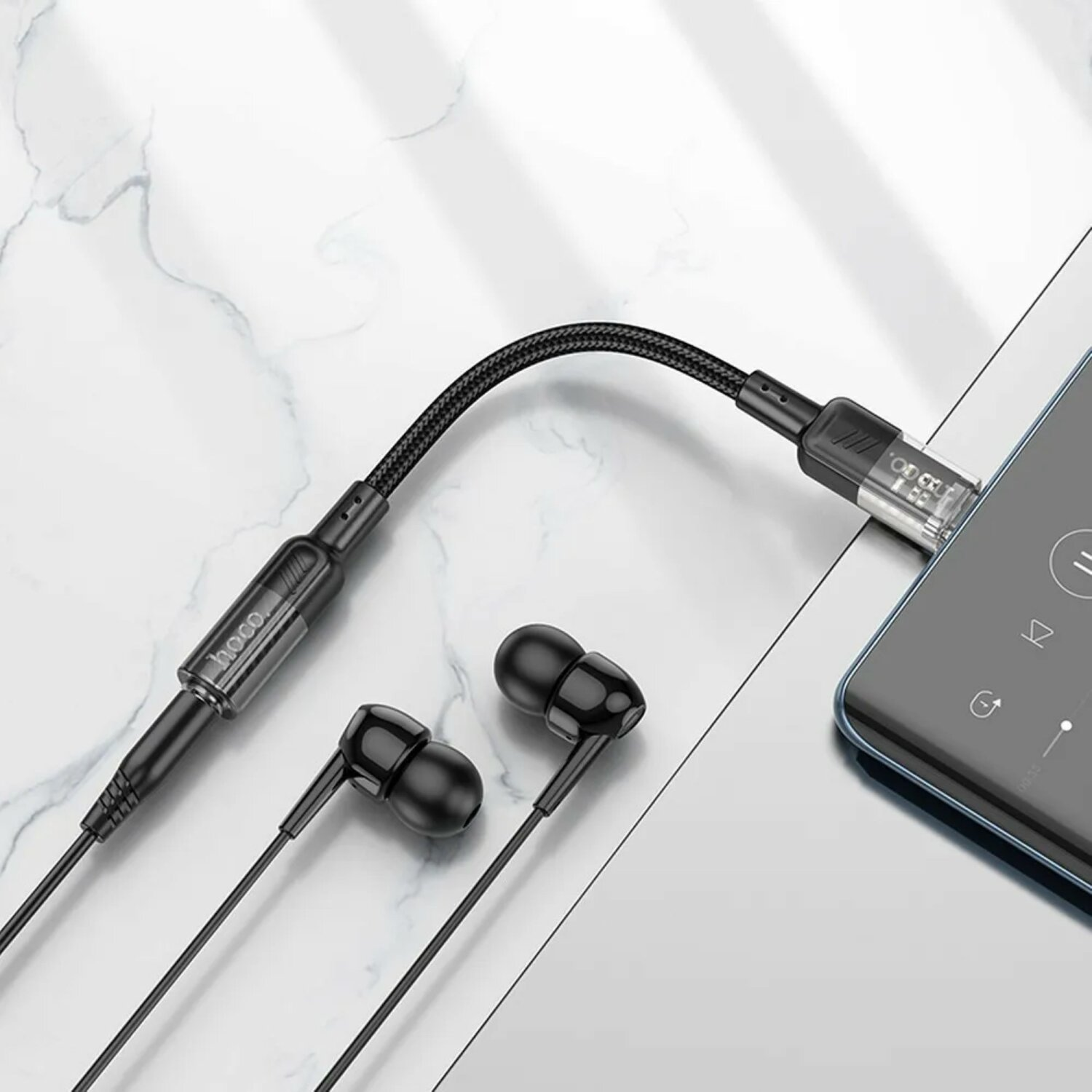 Schwarze Kopfhörer, die mit einem Telefon verbunden sind. Telefon befindet sich auf glänzender Oberfläche.