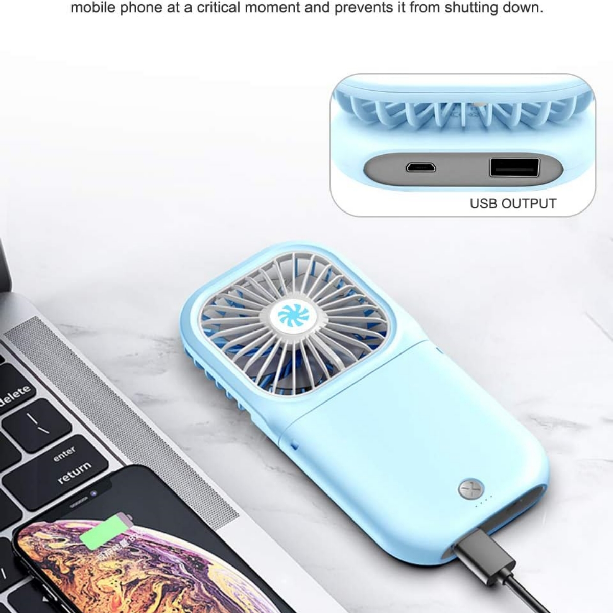 Ein blauer tragbarer Ventilator mit USB-Ausgang, der ein Telefon auf einem Laptop auflädt, neben einer Tastatur.