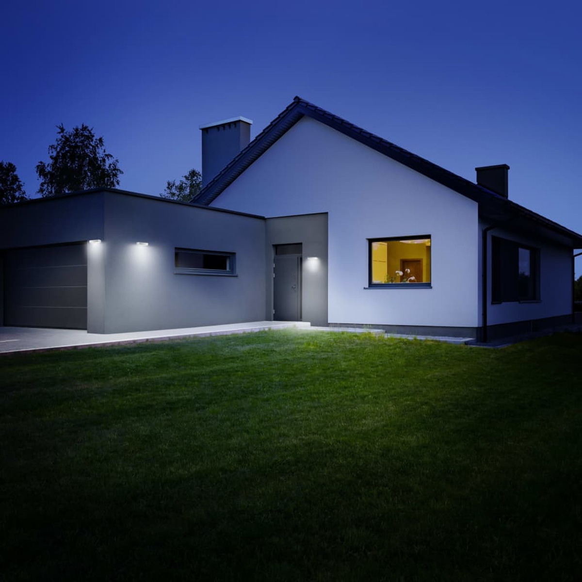 Ein Haus bei Nacht mit Lichtern. Eine Garage ist an der Seite befestigt. Der Himmel ist dunkelblau.