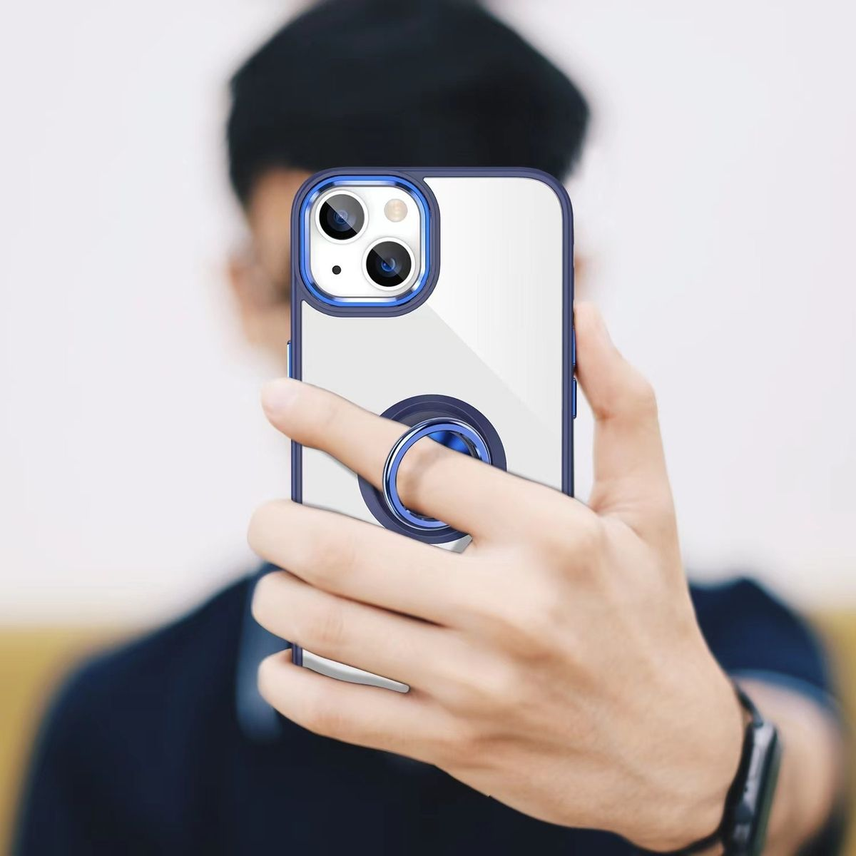 Eine Person, die ein Telefon mit einer blau umrandeten Hülle und einem Ringhalter hält, im Selfie-Stil, vor verschwommenem Hintergrund.