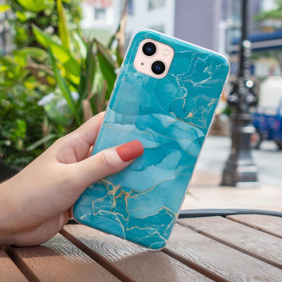 Hand, die ein Telefon mit einer blauen Marmorhülle hält. Der Hintergrund umfasst einen Tisch und unscharfes Grün.