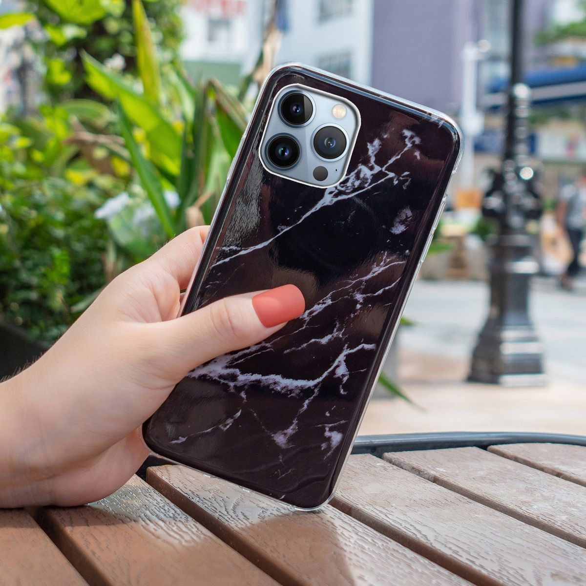 Hand hält Telefon mit Marmorgehäuse. Hintergrund: Straße und verschwommenes Grün.