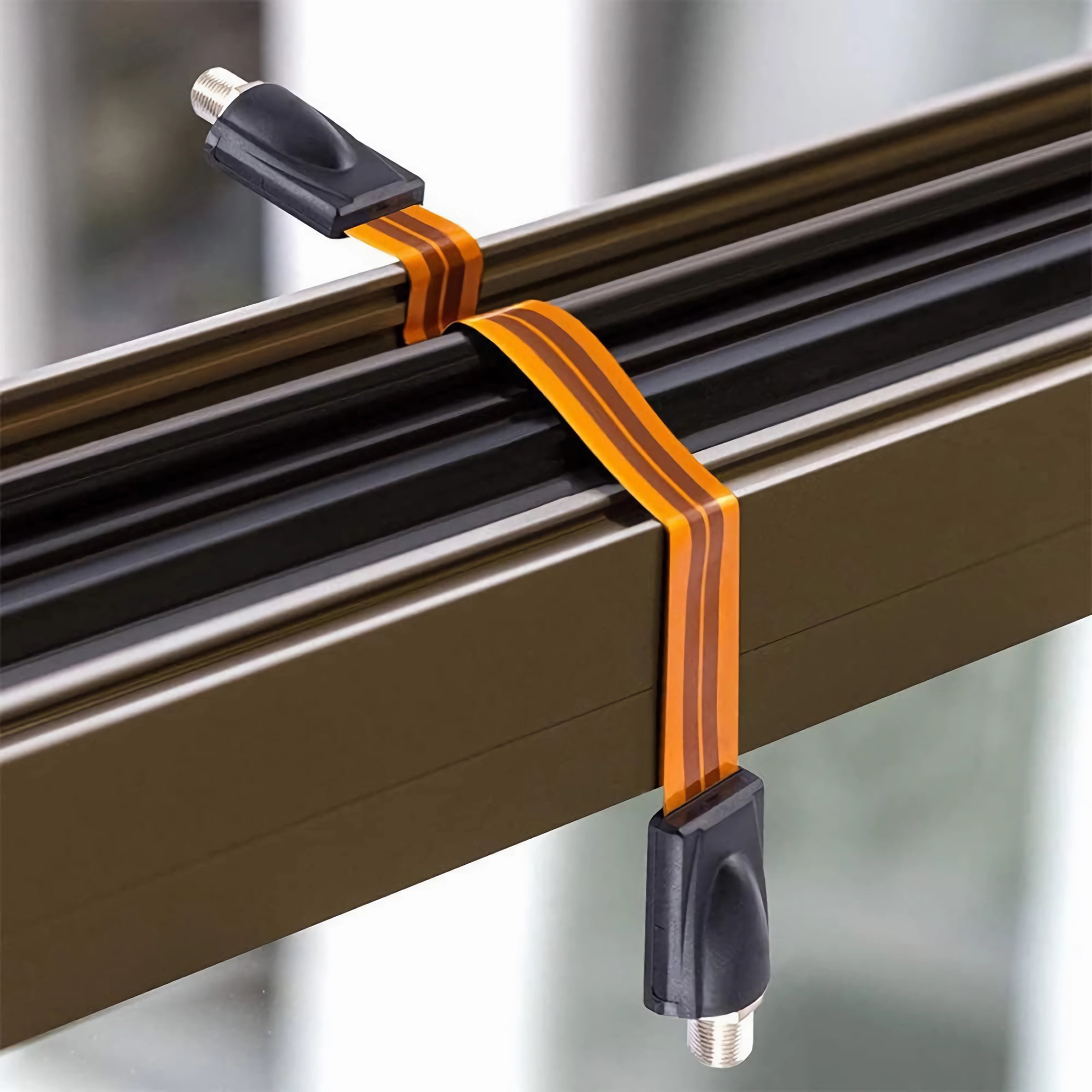 Ein dünnes orangefarbenes Kabel mit zwei schwarzen Steckern. Es befindet sich auf einer Metallstruktur.