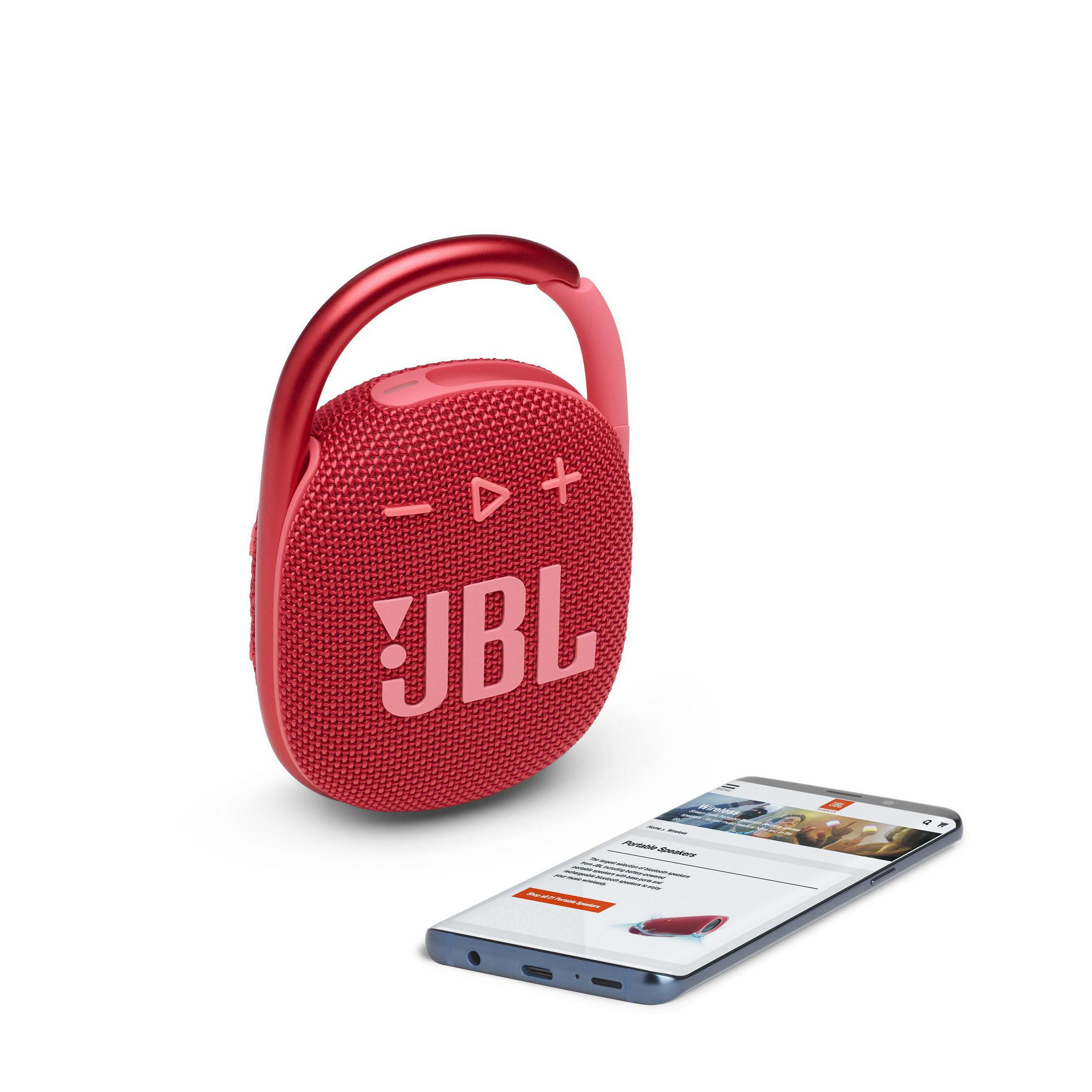 Un altavoz JBL rojo con asa y un teléfono inteligente que muestra un sitio web. Fondo blanco.