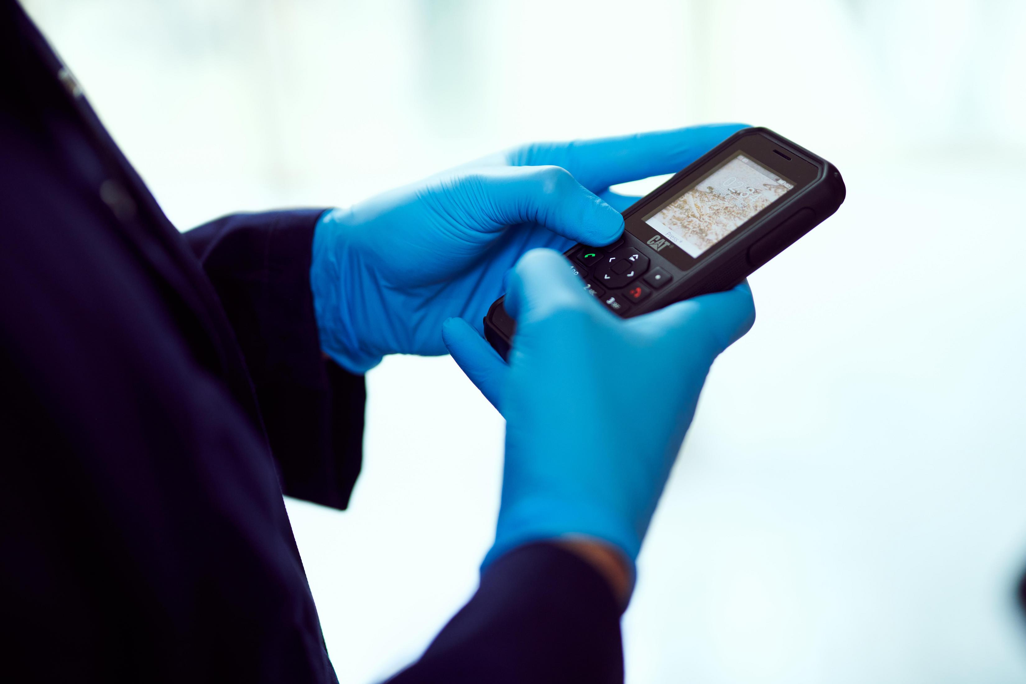Osoba w niebieskich rękawicach trzymająca czarny telefon z widocznym ekranem.