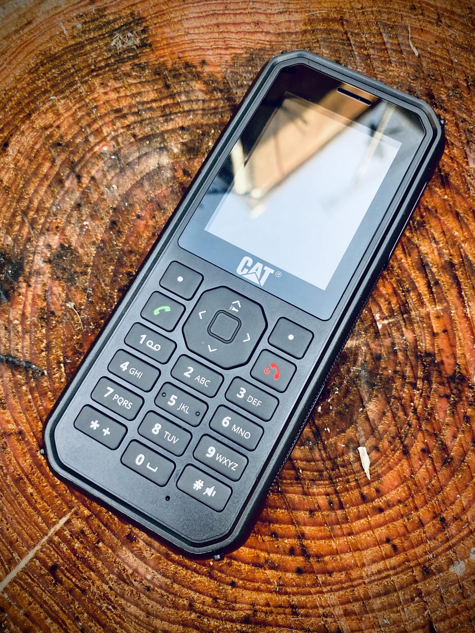 Czarny, wytrzymały telefon CAT na drewnianej powierzchni. Posiada klawiaturę i ekran.