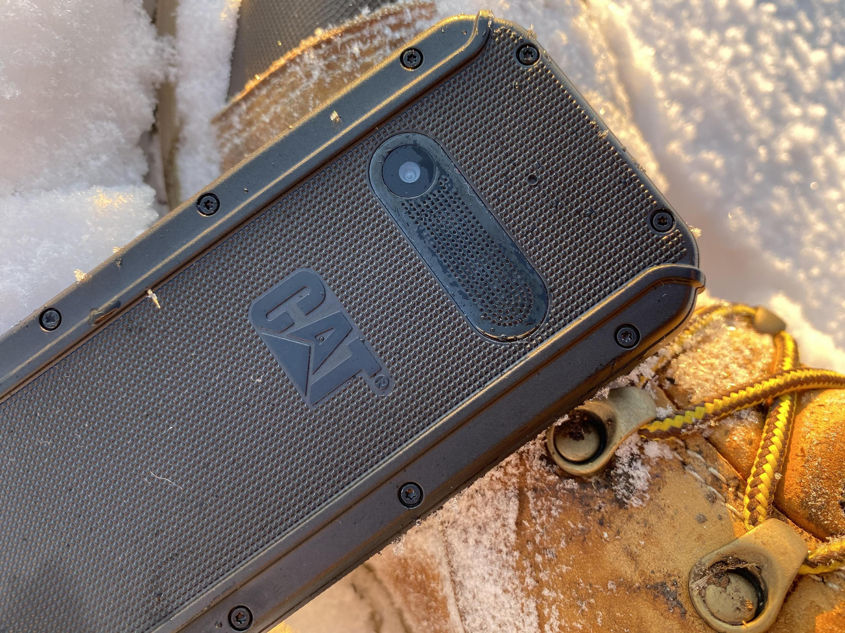 Zbliżenie czarnego, wytrzymałego telefonu z logo CAT na śniegu i bucie.