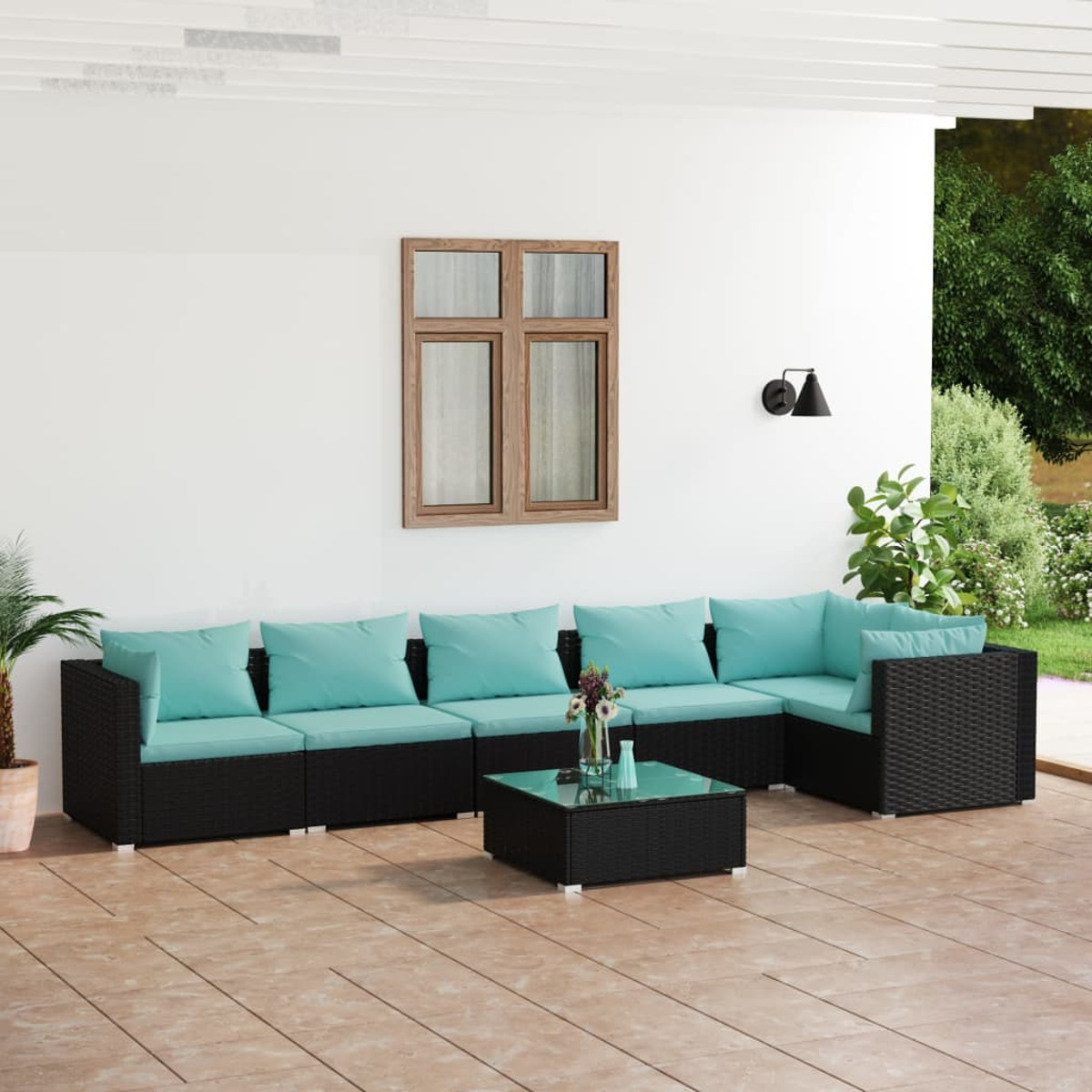 Gartenmöbel-Set mit schwarzem Korbgeflecht und blauen Kissen. Weiße Wand und gepflasterter Boden.