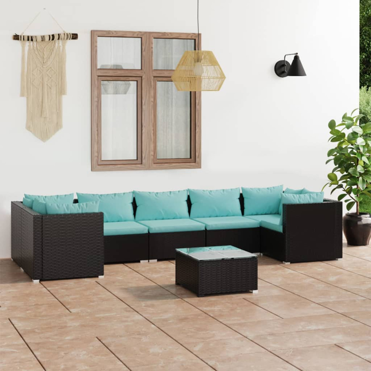 Außenbereich mit Sitzgelegenheiten. Ein schwarzes Korbsessel-Sofa mit türkisfarbenen Kissen, einem Tisch und Pflanzen.