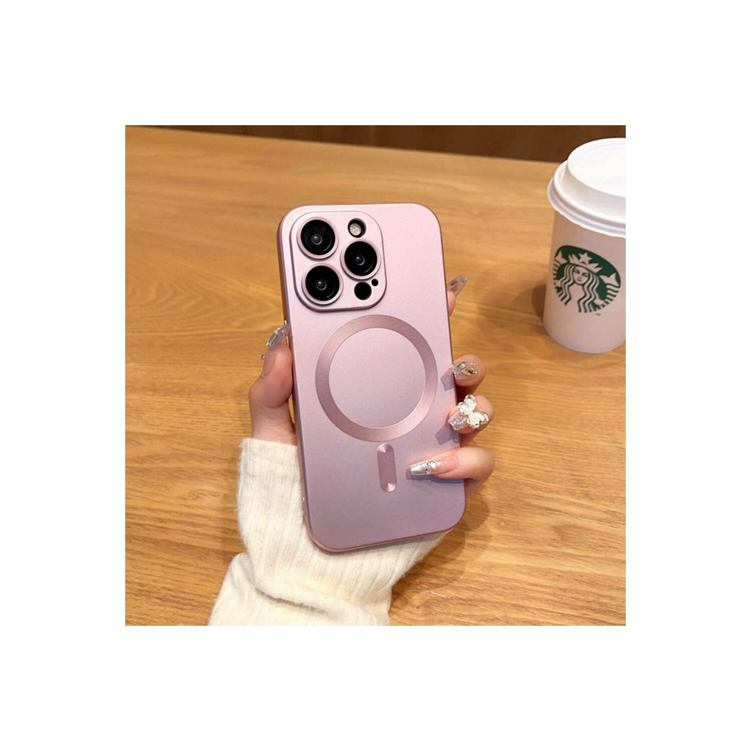 La mano di una persona che tiene una custodia rosa per telefono con una tazza di caffè bianca sullo sfondo su un tavolo di legno.