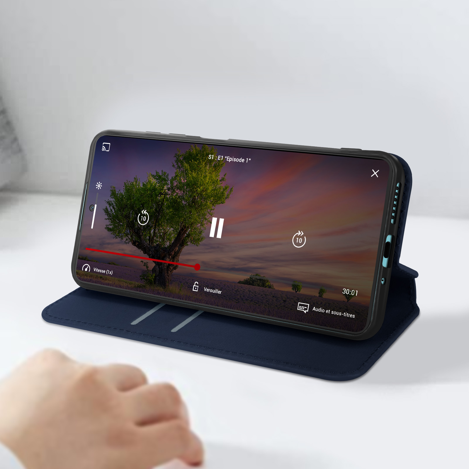Telefono in una custodia blu, che mostra un video. Una mano è vicino allo schermo. Il video mostra un albero.