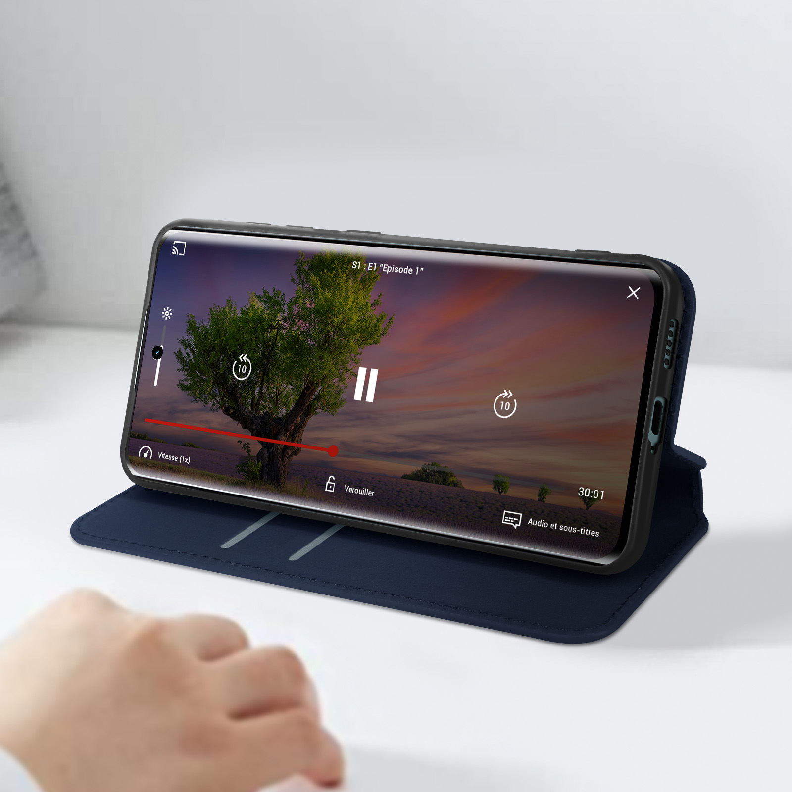 Un telefono in una custodia blu mostra un video di un albero, con una mano sulla custodia.