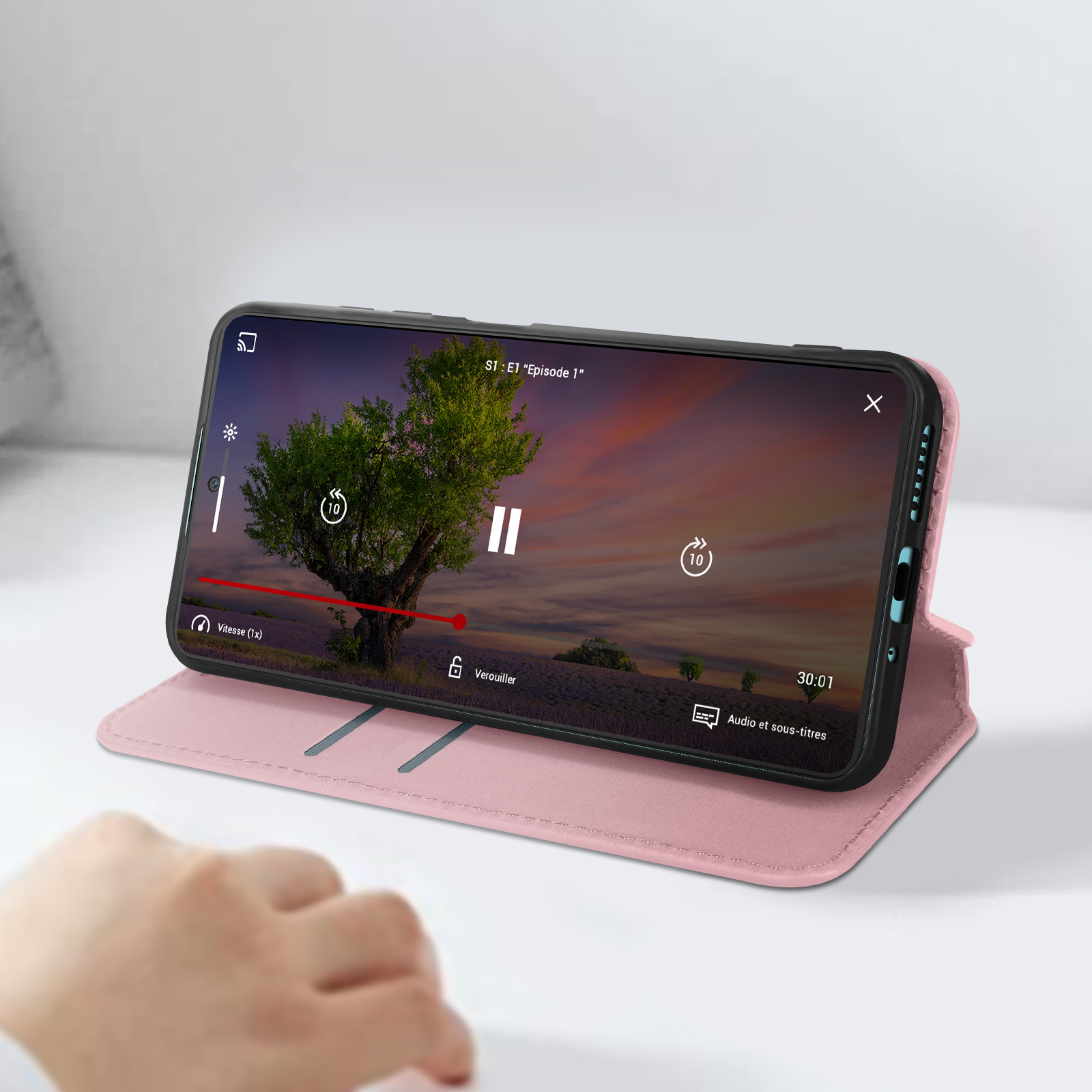 Un telefono mostra un video, appoggiato aperto in una custodia rosa su una superficie bianca.