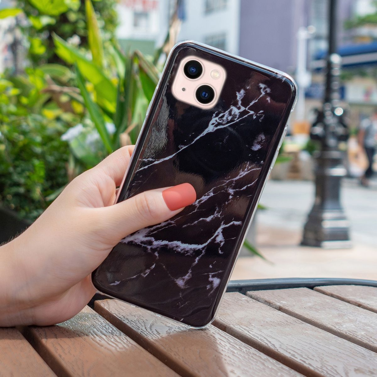Eine Hand, die ein Telefon mit Marmormuster hält, mit verschwommenem Hintergrund einer Straßenszene.
