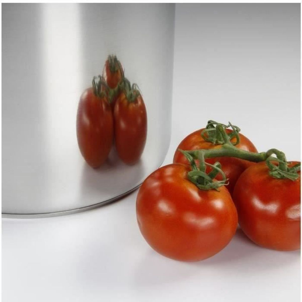 Tomaten neben einem Stahltopf. Drei Tomaten an einer Ranke und deren Spiegelung im Topf.