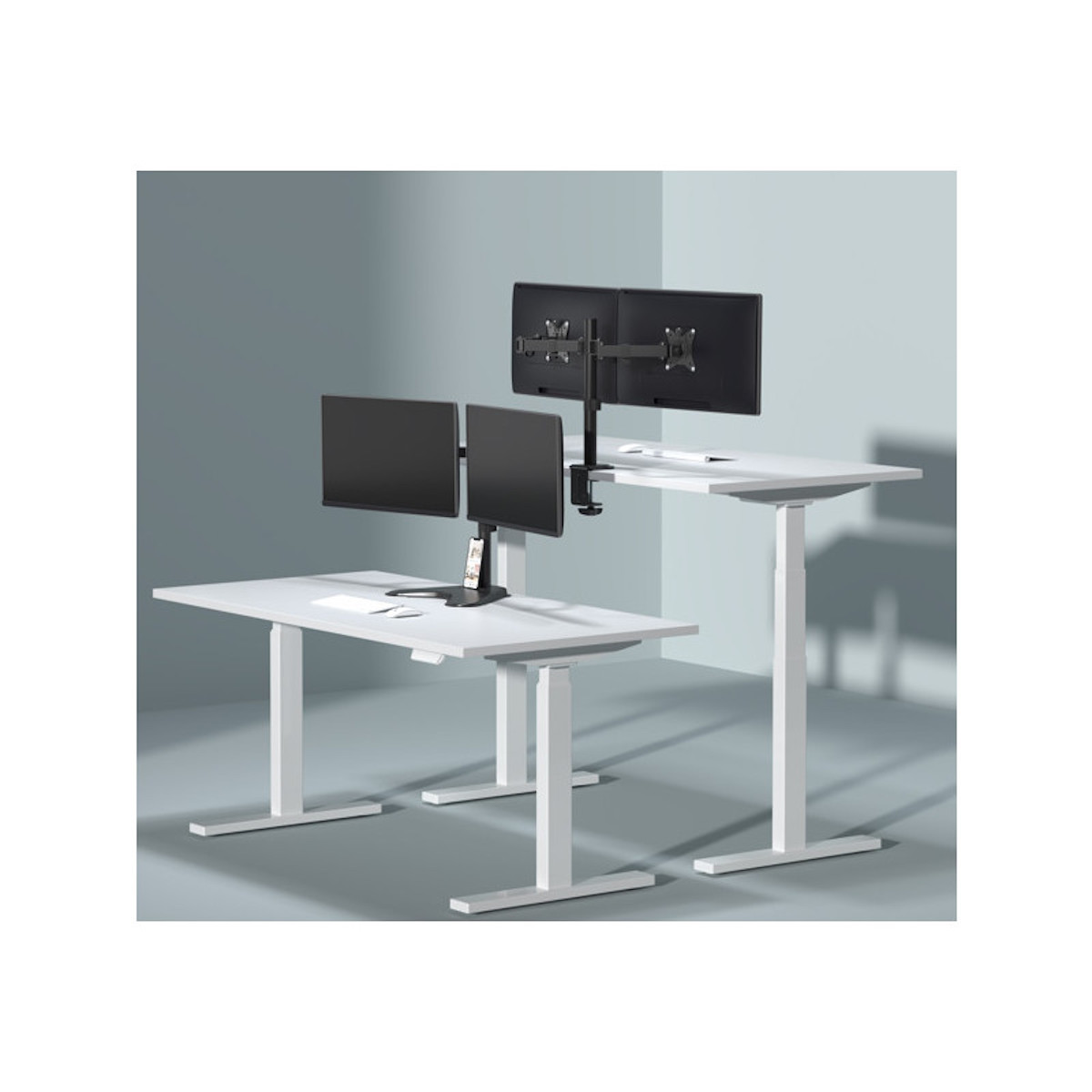 Zwei weiße Schreibtische mit Monitoren und einem Monitorständer, alles vor grauem Hintergrund.