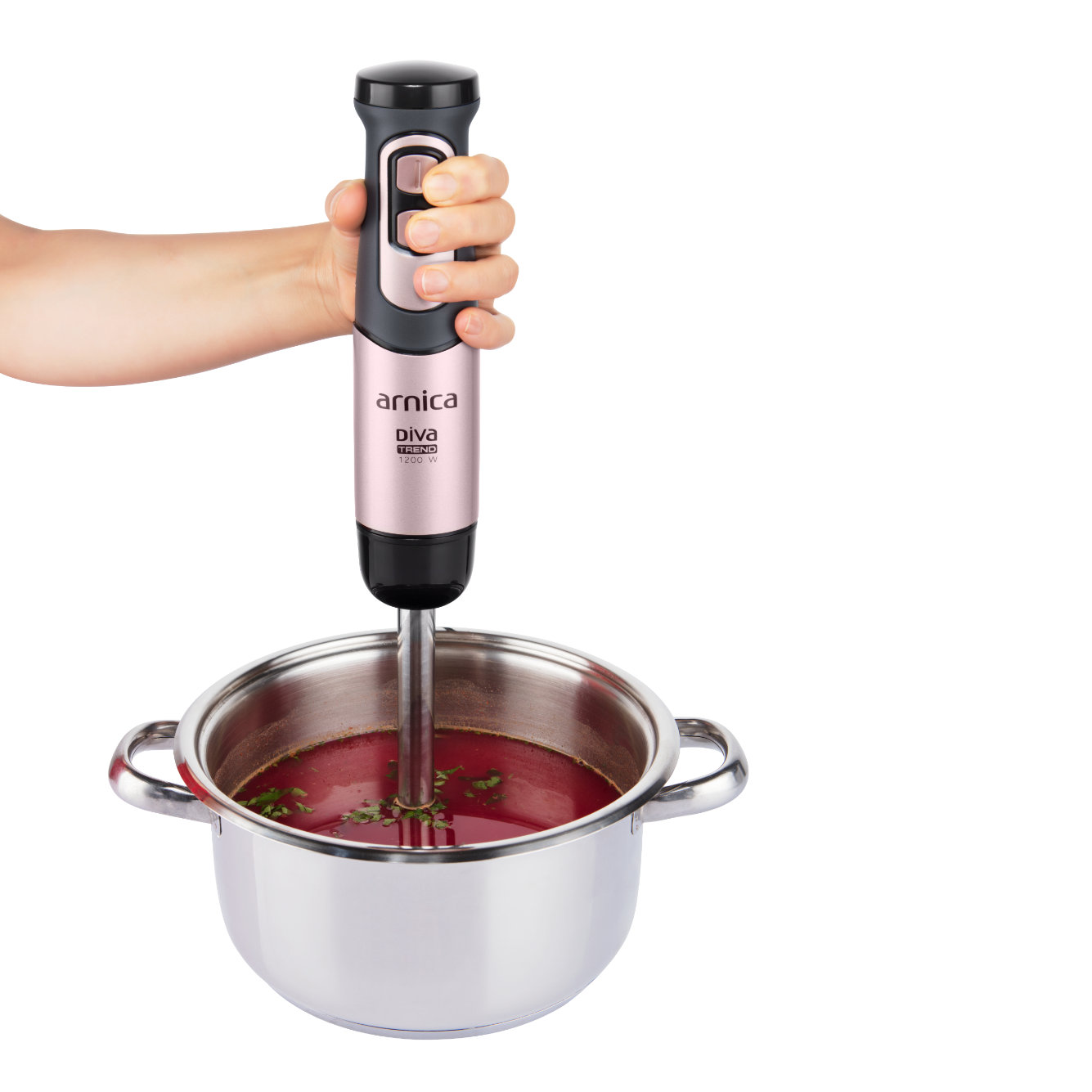 Eine Hand, die einen rosa Stabmixer über einem Topf mit roter Flüssigkeit hält.