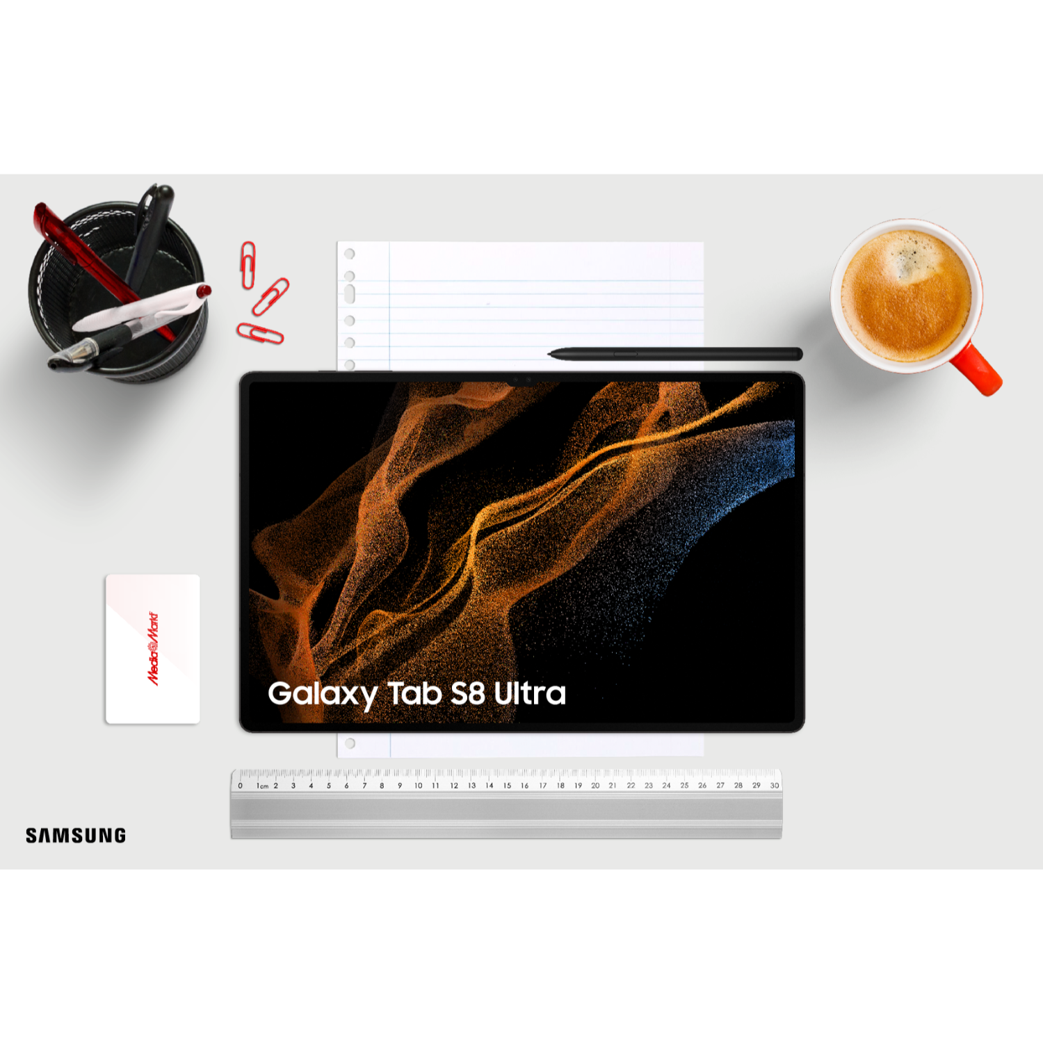 Una tableta con pantalla negra, rodeada de útiles de oficina sobre una superficie blanca, vista superior.