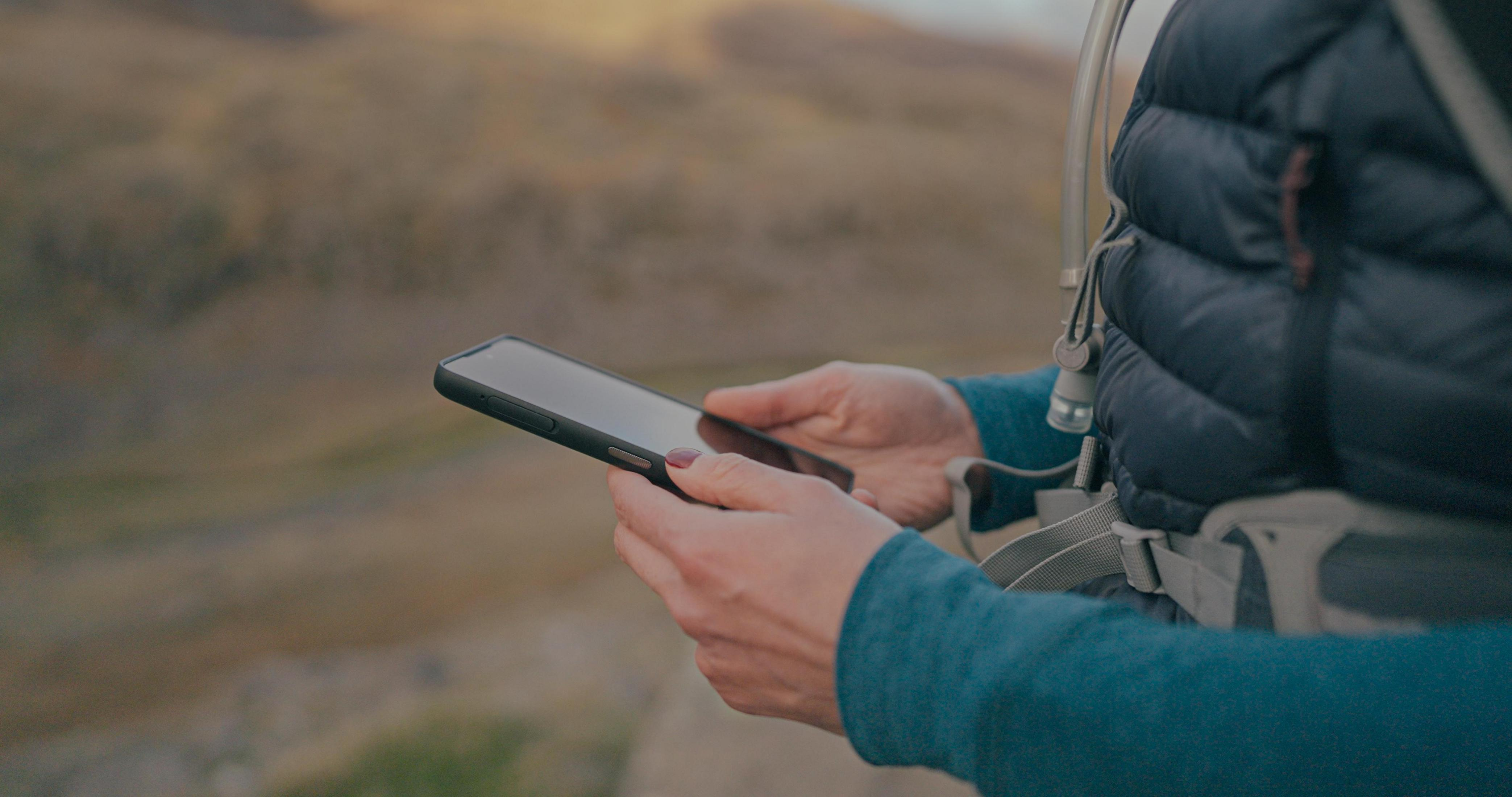 Eine Person hält ein Telefon. Sie sind draußen auf einem Berg. Sie halten das Telefon und schauen es an.