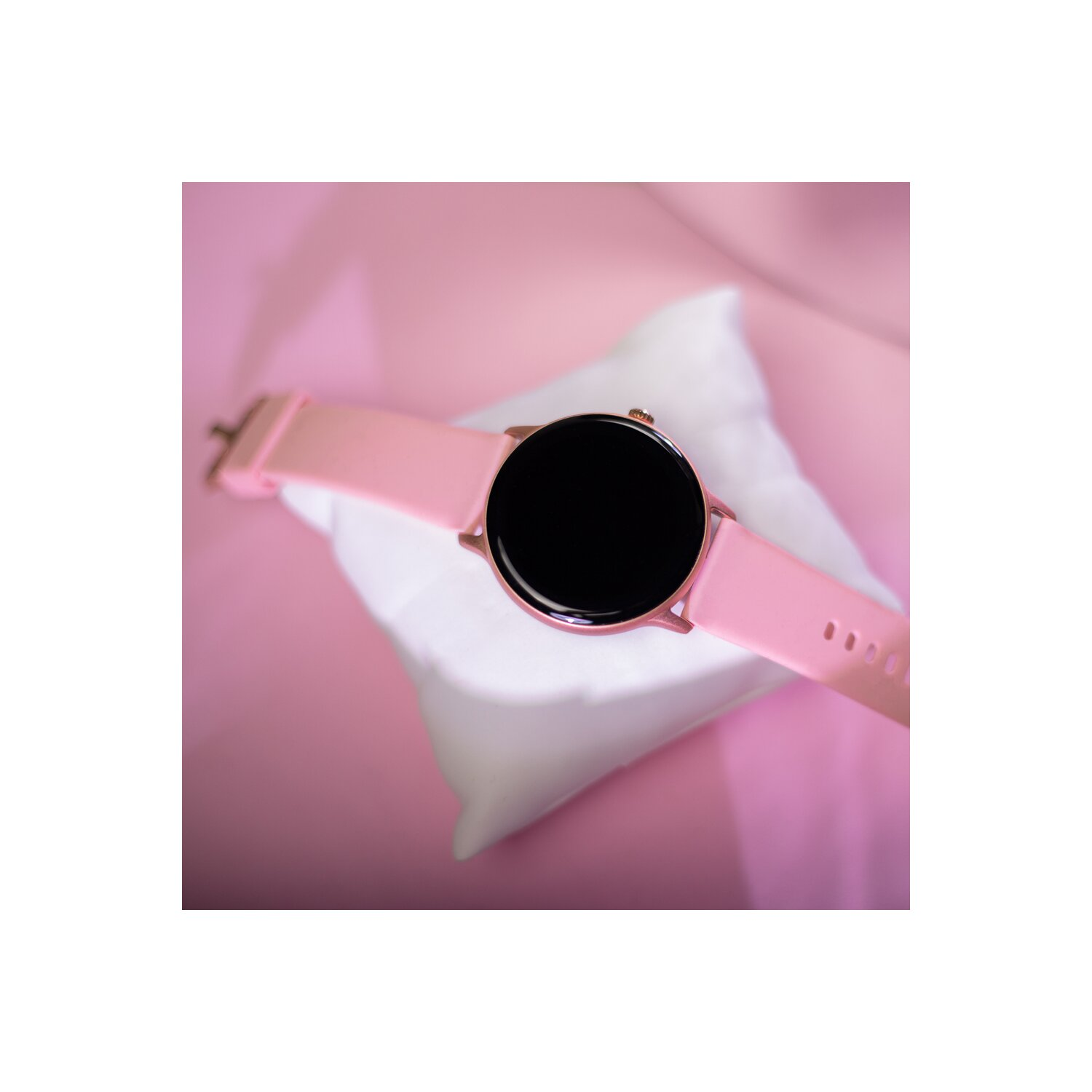 Pinke Smartwatch auf weißem Kissen, auf pinkem Hintergrund. Schwarzer Bildschirm.