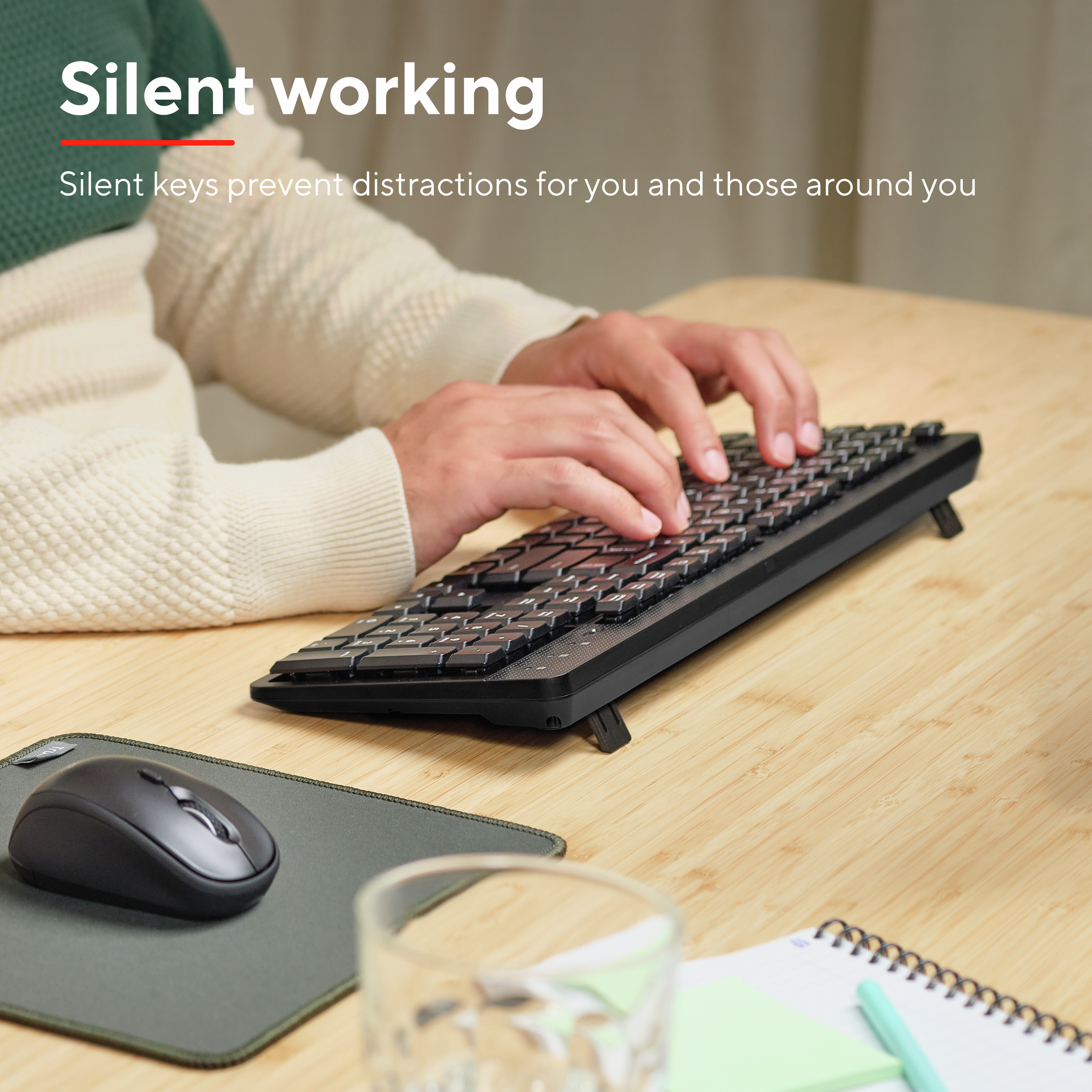 Dłonie piszące na czarnej klawiaturze z myszką i szklanką.