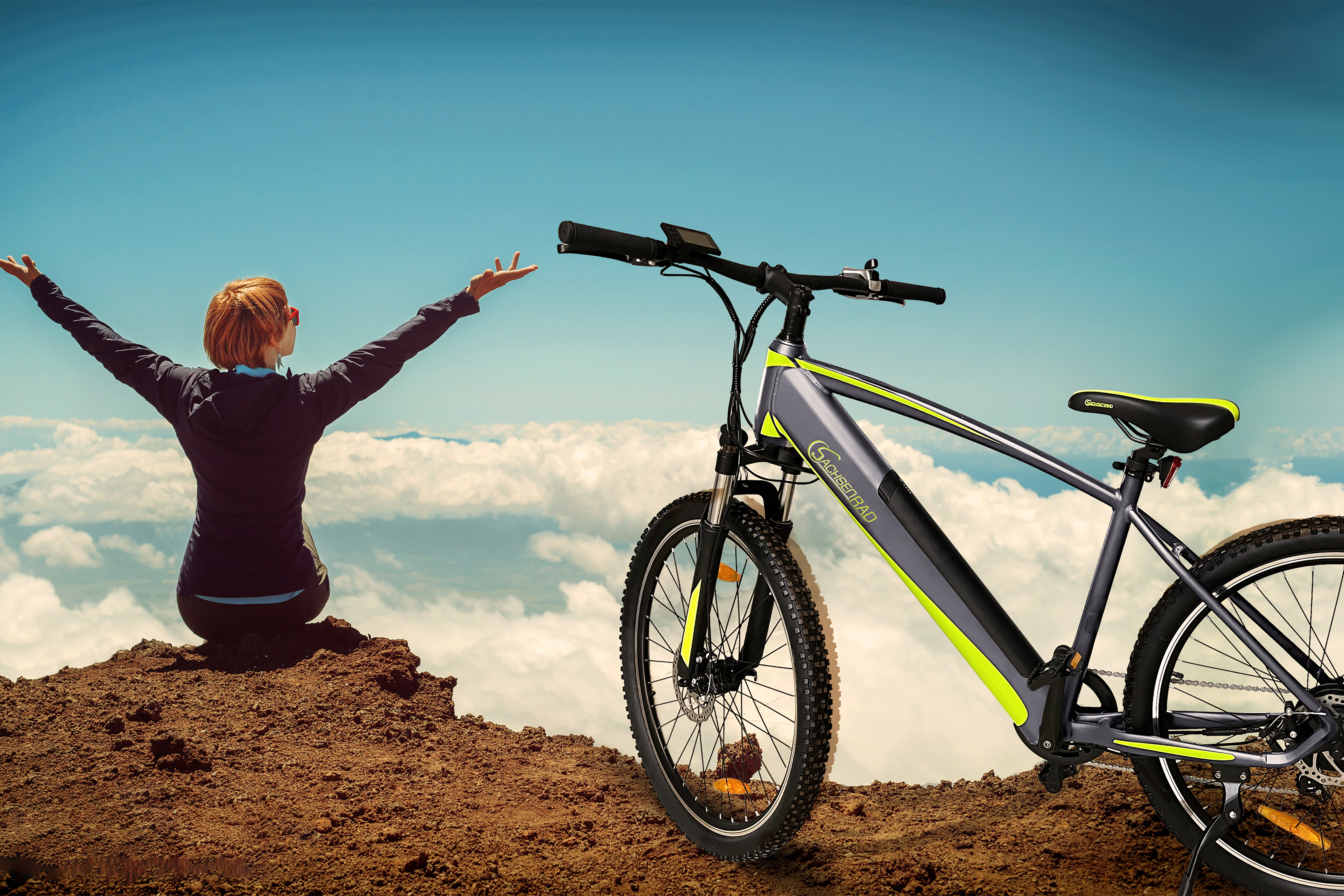 Frau mit erhobenen Armen auf einem Berg mit einem Elektrofahrrad.