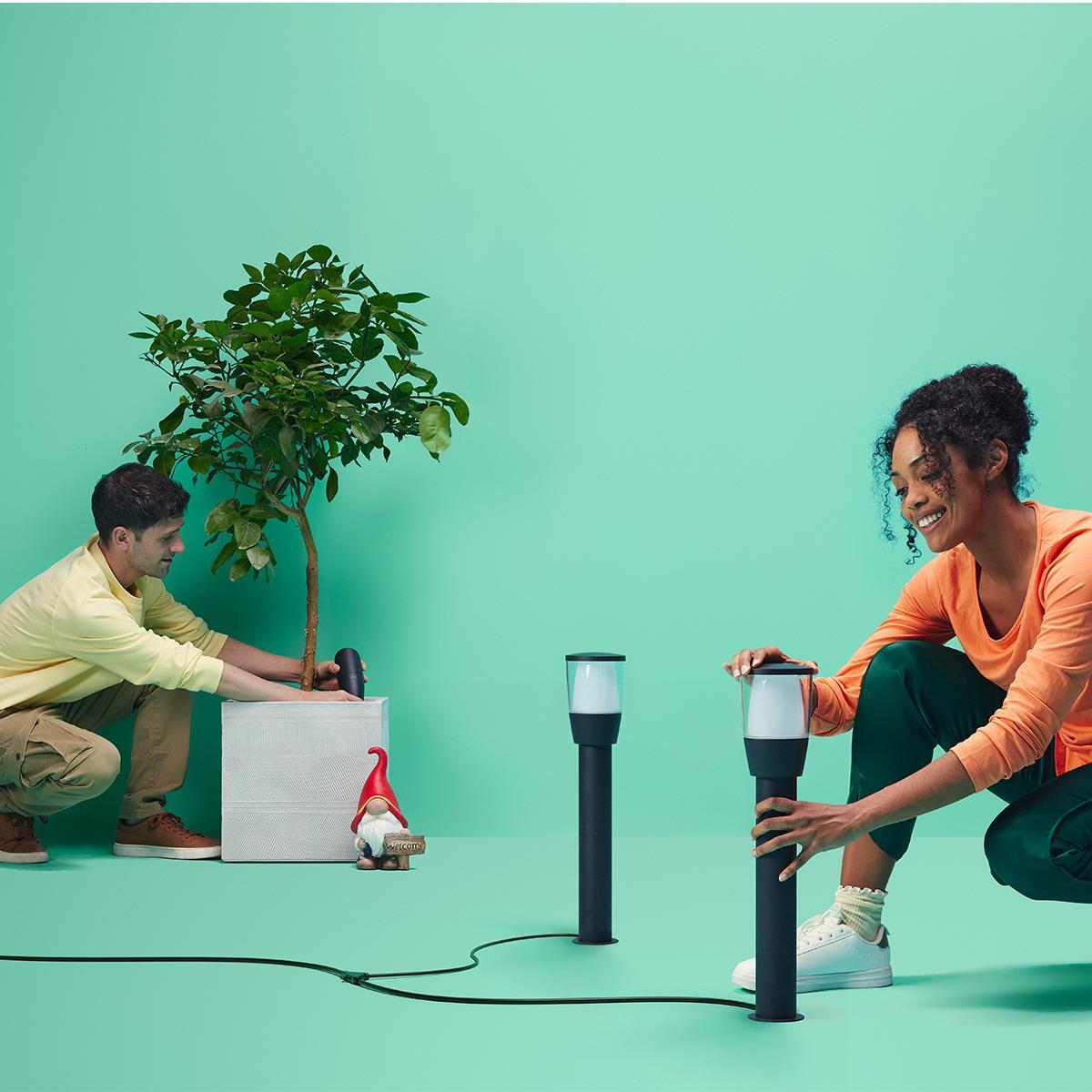 Deux personnes installent des lampes d'extérieur. Ils sont sur une surface verte. Il y a une plante.