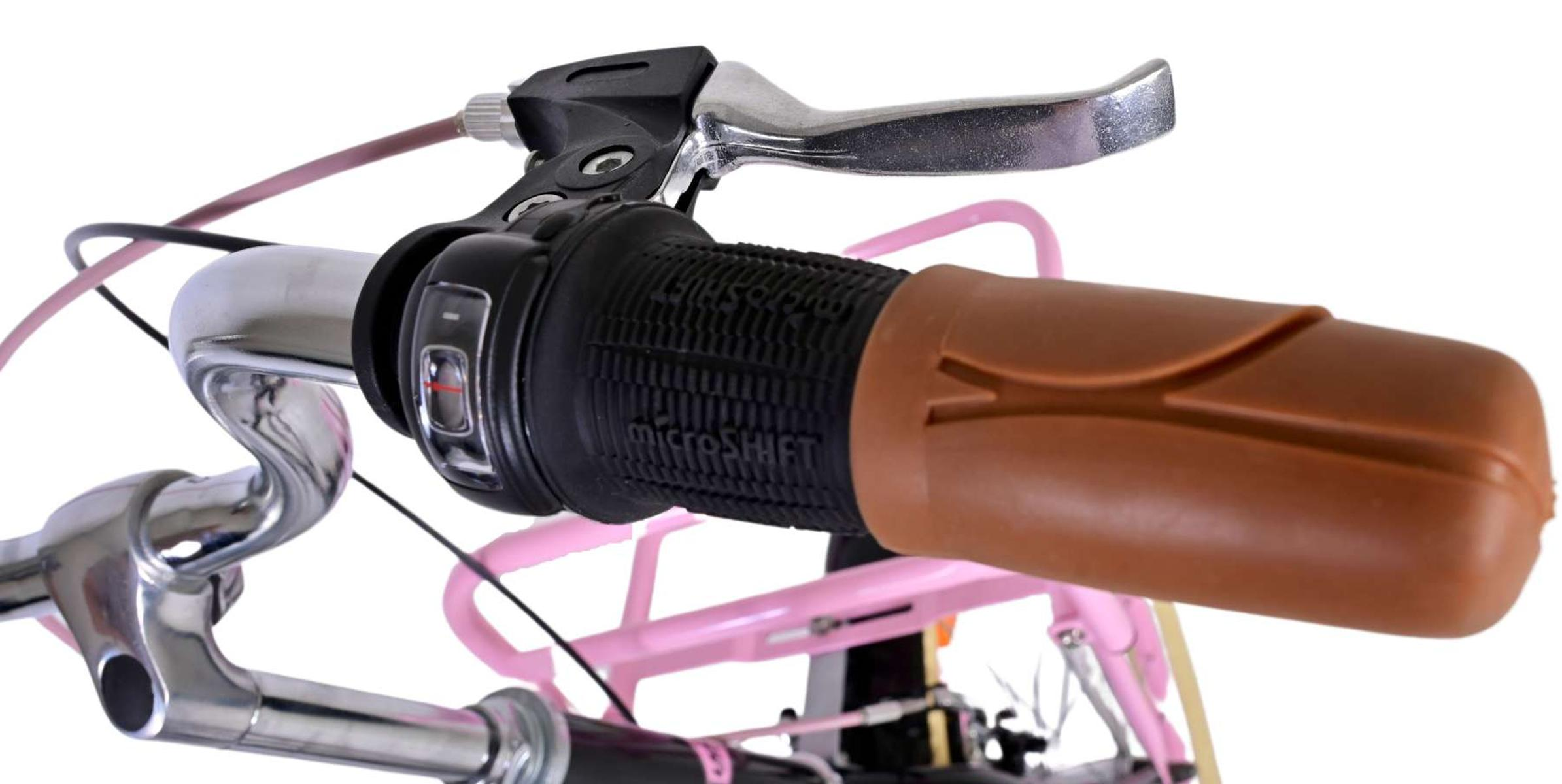 Fahrradlenker, brauner Griff, schwarze Bedienelemente. Pinker Rahmen sichtbar.