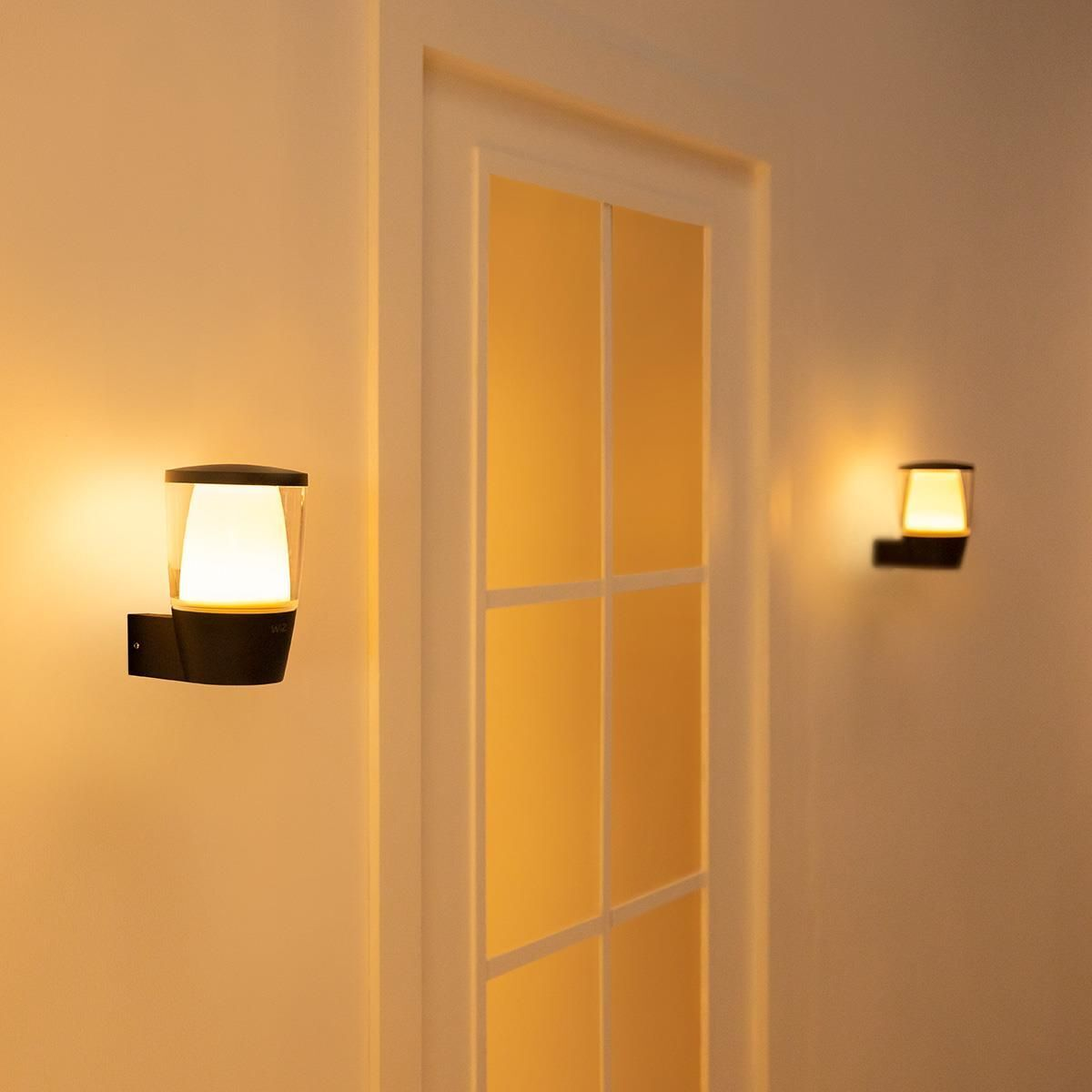 Deux appliques murales. Base noire, lumière blanche. Une de chaque côté d'une porte.