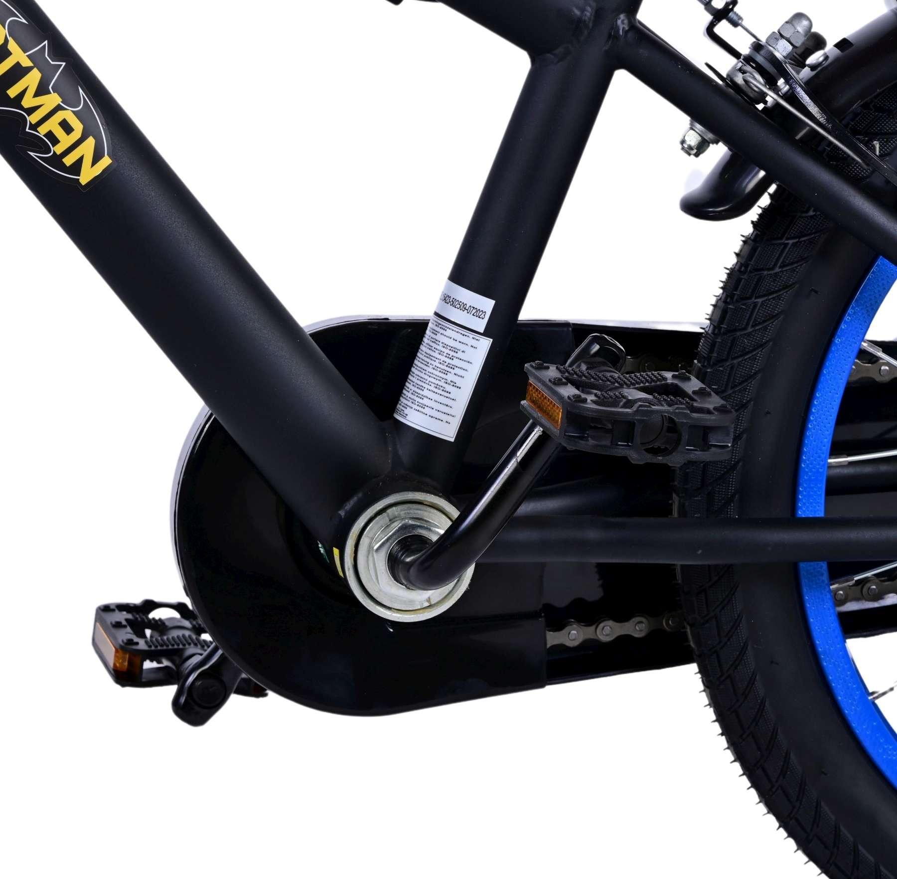 Nahaufnahme eines schwarzen und gelben Batman-Fahrrads. Details von Pedalen, Kette und Reifen auf weißem Hintergrund.