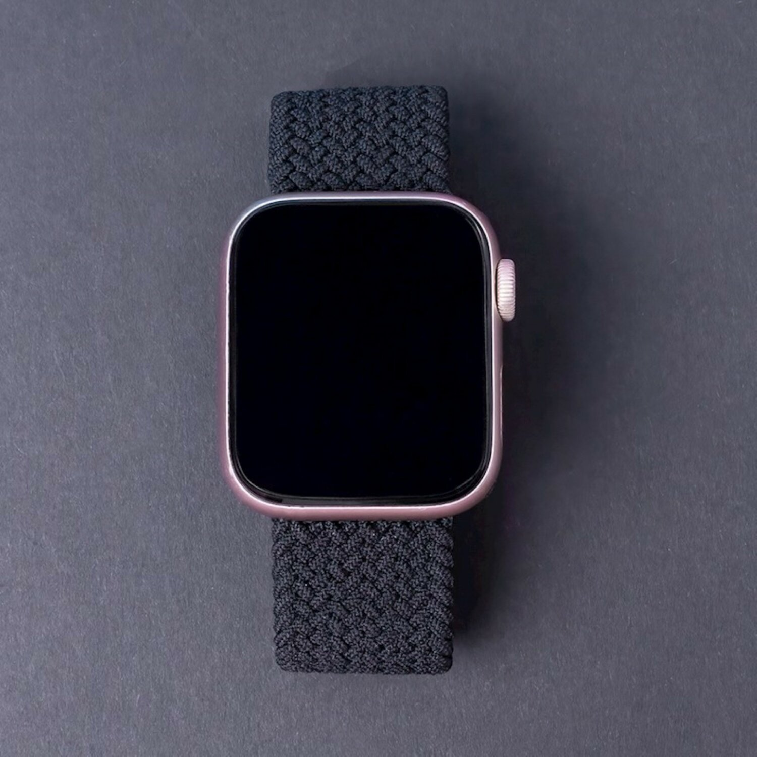 Eine Apple Watch mit schwarzem Bildschirm und einem schwarzen, gewebten Armband. Das Gehäuse hat Roségold.
