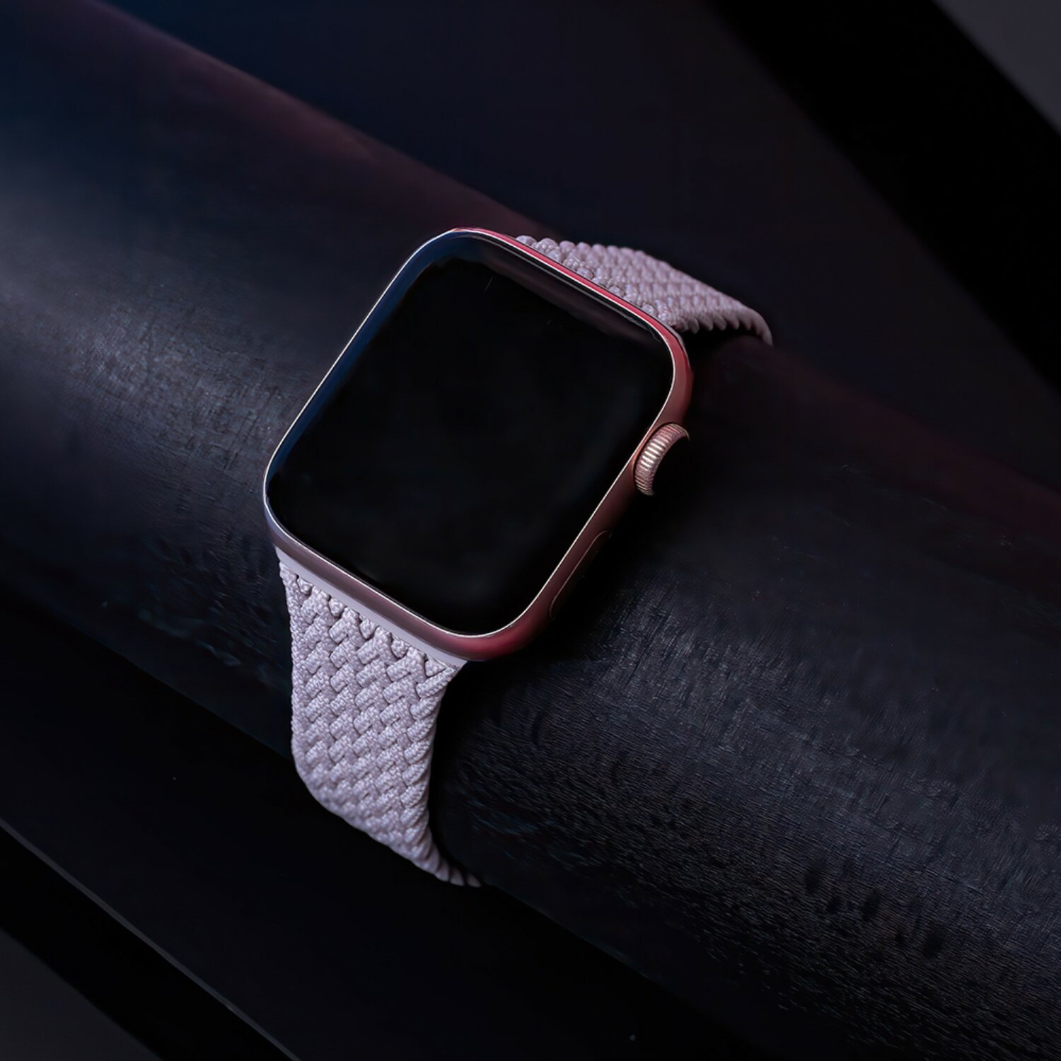 Eine roségoldene Smartwatch mit schwarzem Bildschirm und grauem geflochtenem Armband. Auf dunkler Oberfläche.
