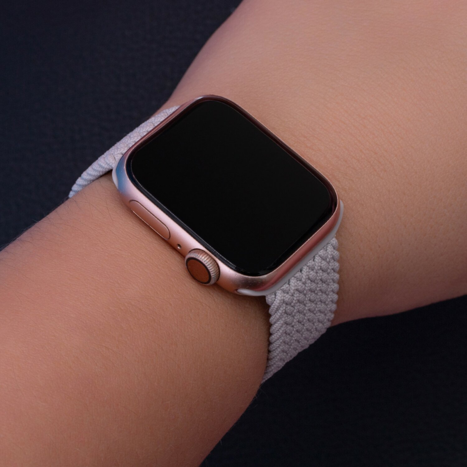 Nahaufnahme einer roségoldenen Apple Watch am Handgelenk mit grauem Band.