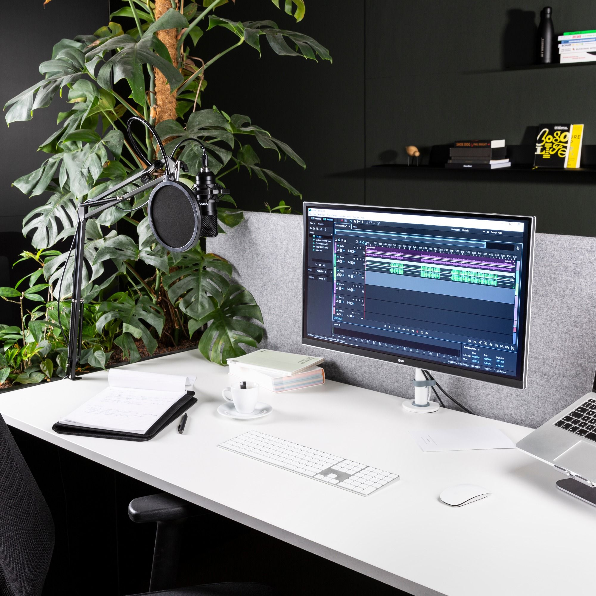 Werkplek met een computerscherm, microfoon op een standaard en kantoorbenodigdheden.