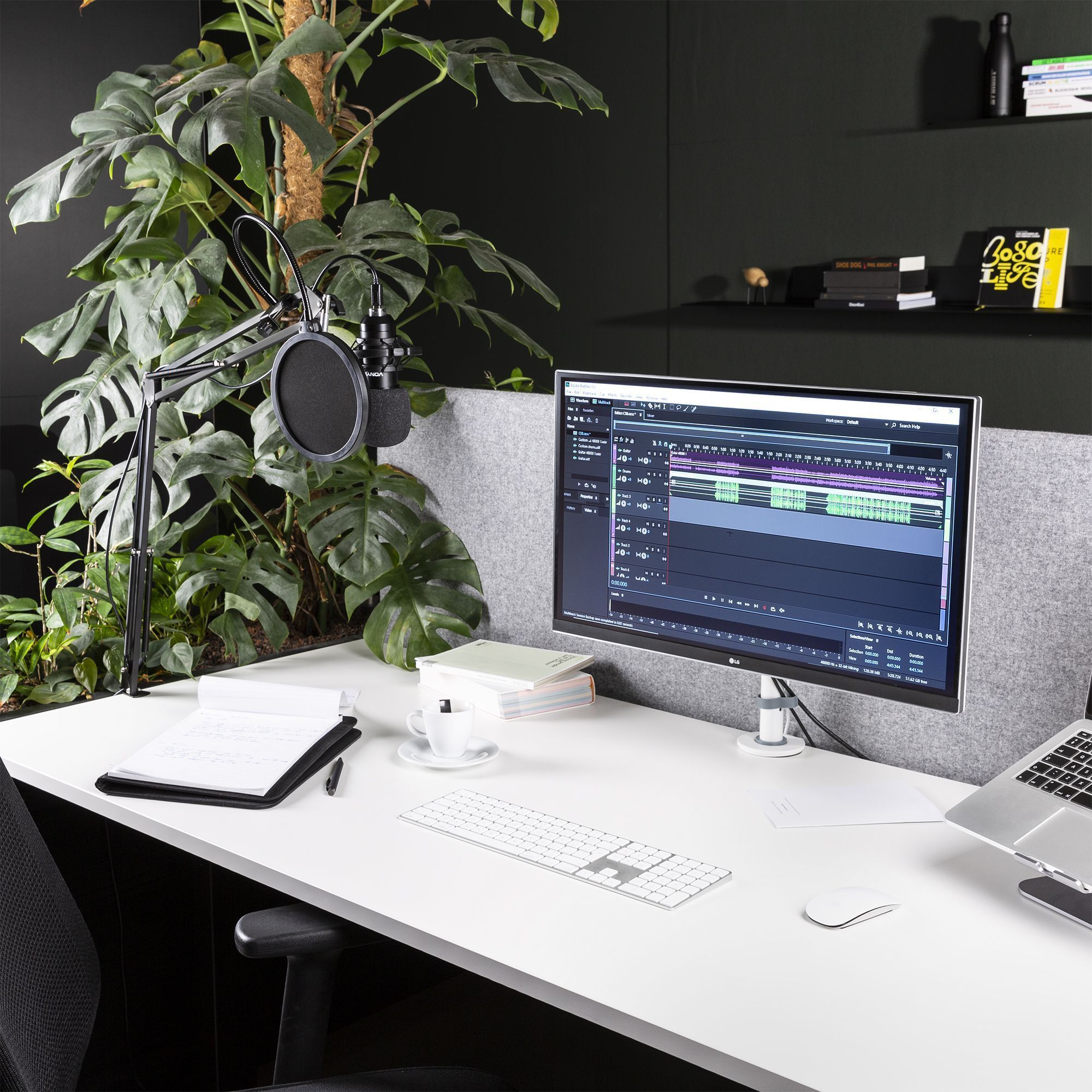Bureau met computer, microfoon, toetsenbord en plant.