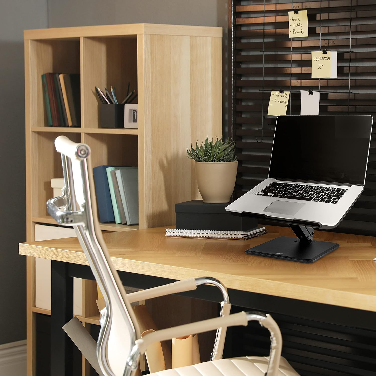 Büro-Setup mit Laptop auf einem Ständer, Büchern und einem Holzschrank. Ein Stuhl steht davor.