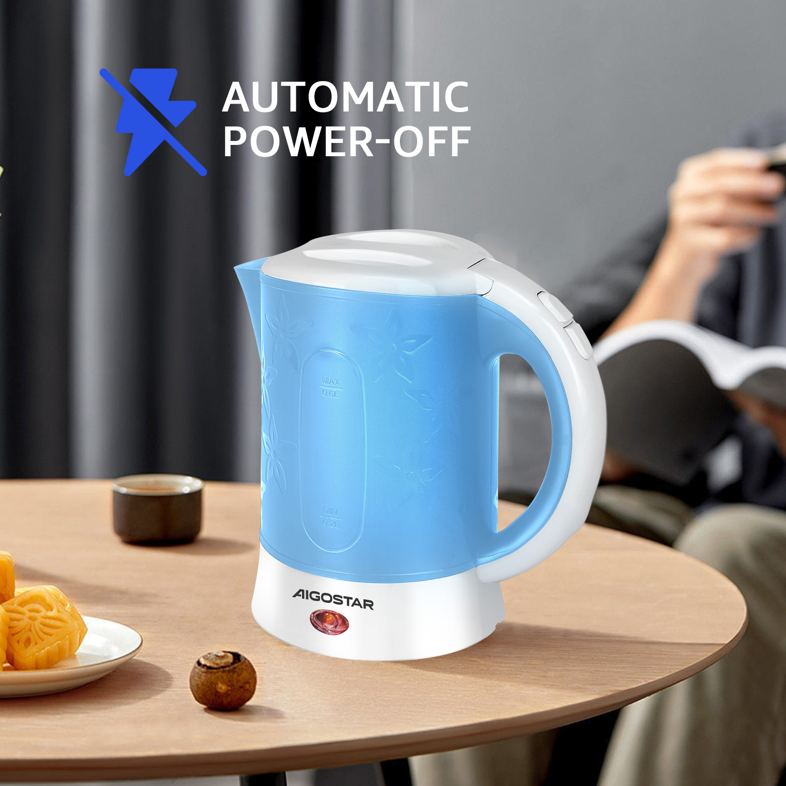 Blauer Wasserkocher mit weißen Akzenten, floralem Design, auf einem Tisch mit Essen und Person im Hintergrund.