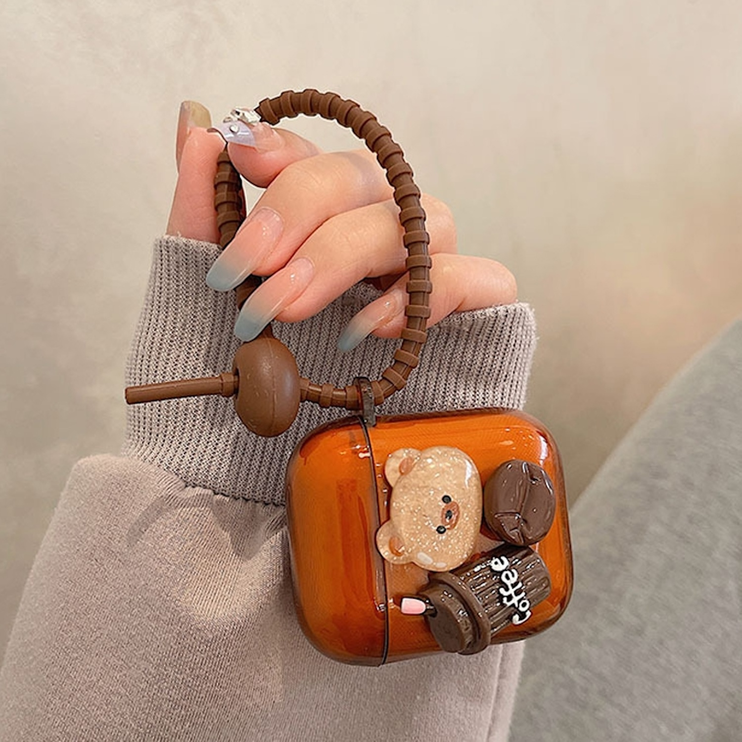 Hand hält eine Handyhülle mit einem Bären- und Kaffeetassen-Design. Braune und orange Farben.