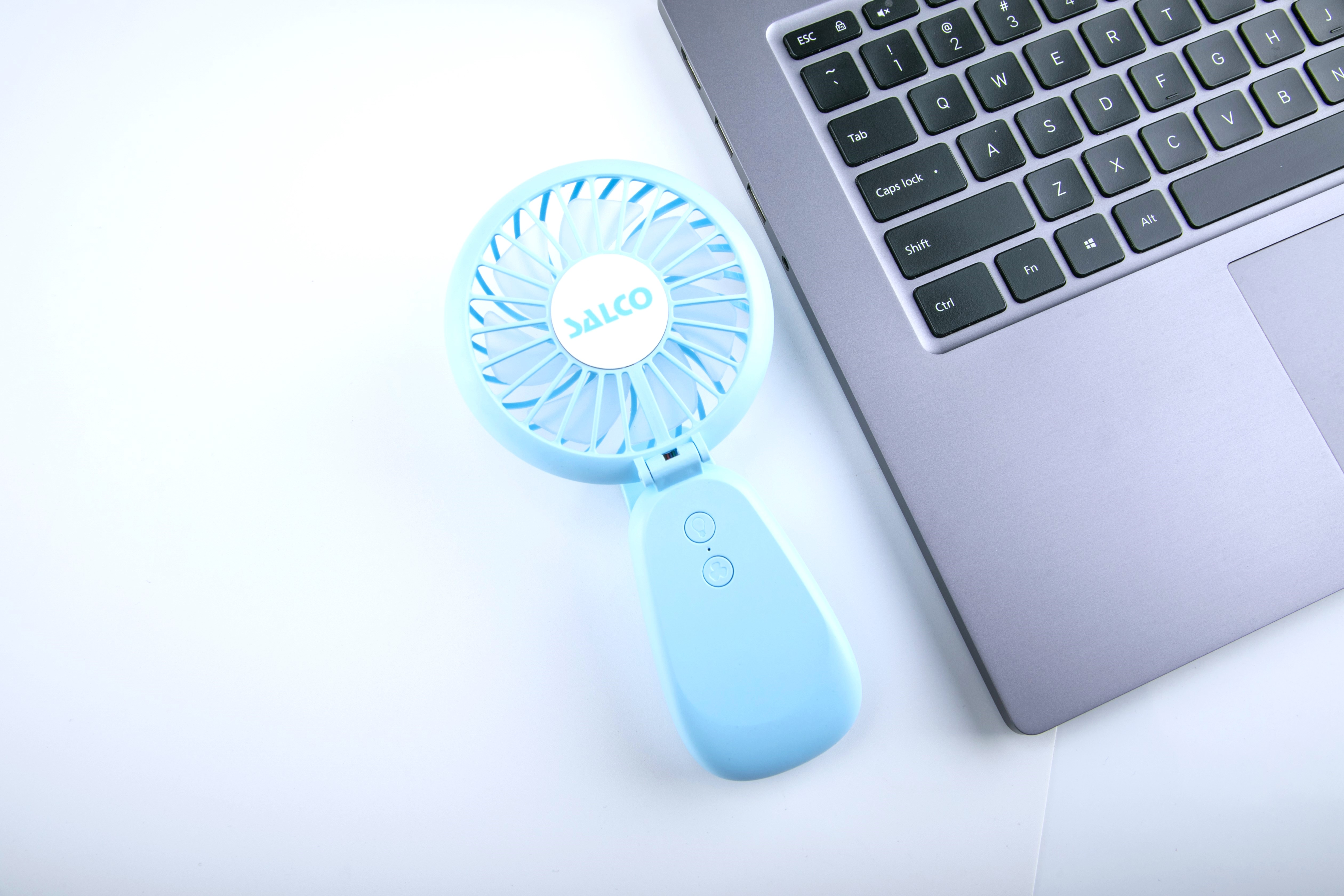 Blauer tragbarer Ventilator auf weißer Oberfläche neben einem Laptop.