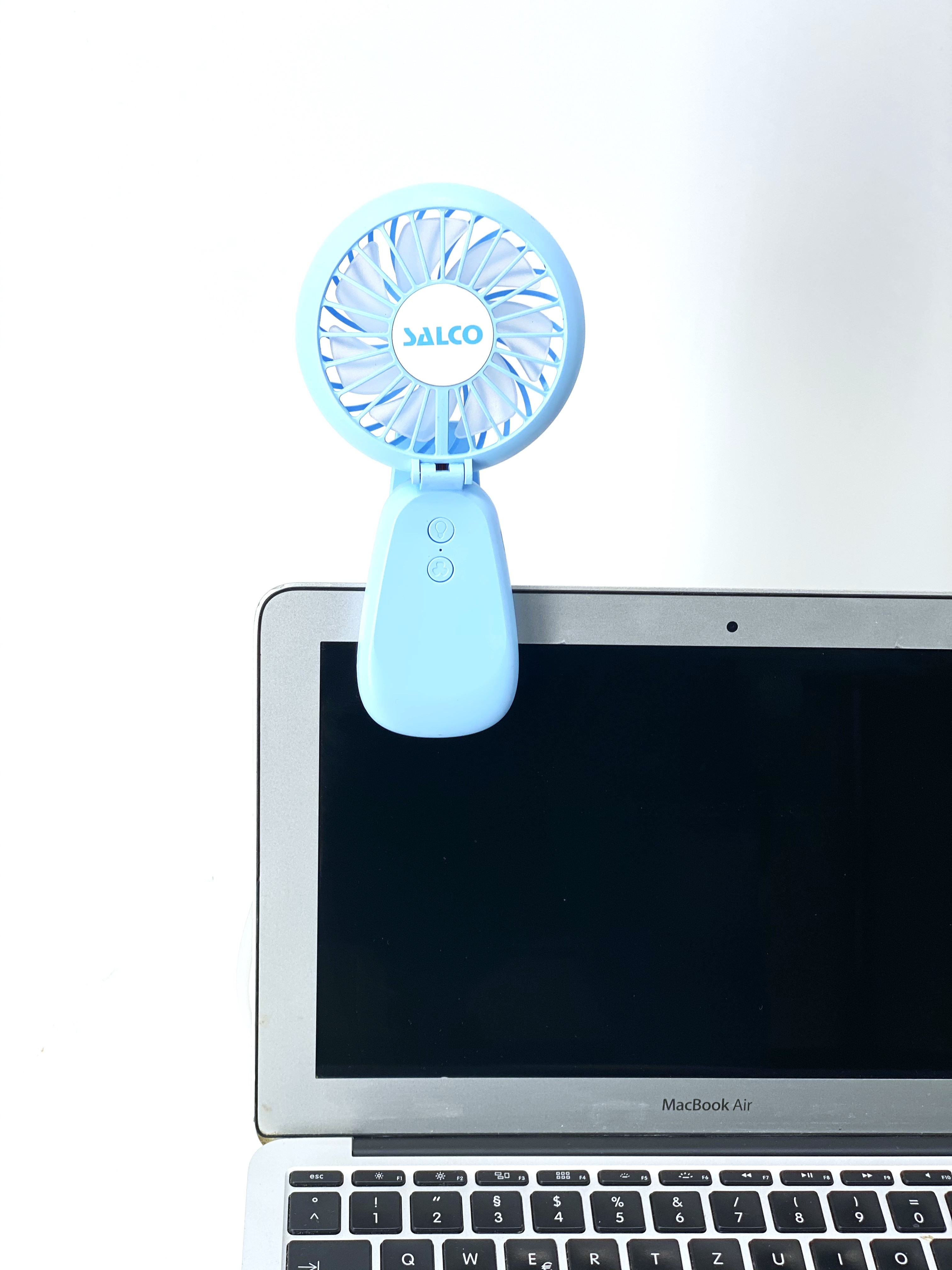 Hellblauer Mini-Ventilator, an einem Laptop befestigt, mit weißem Hintergrund. Der Ventilator ist an.