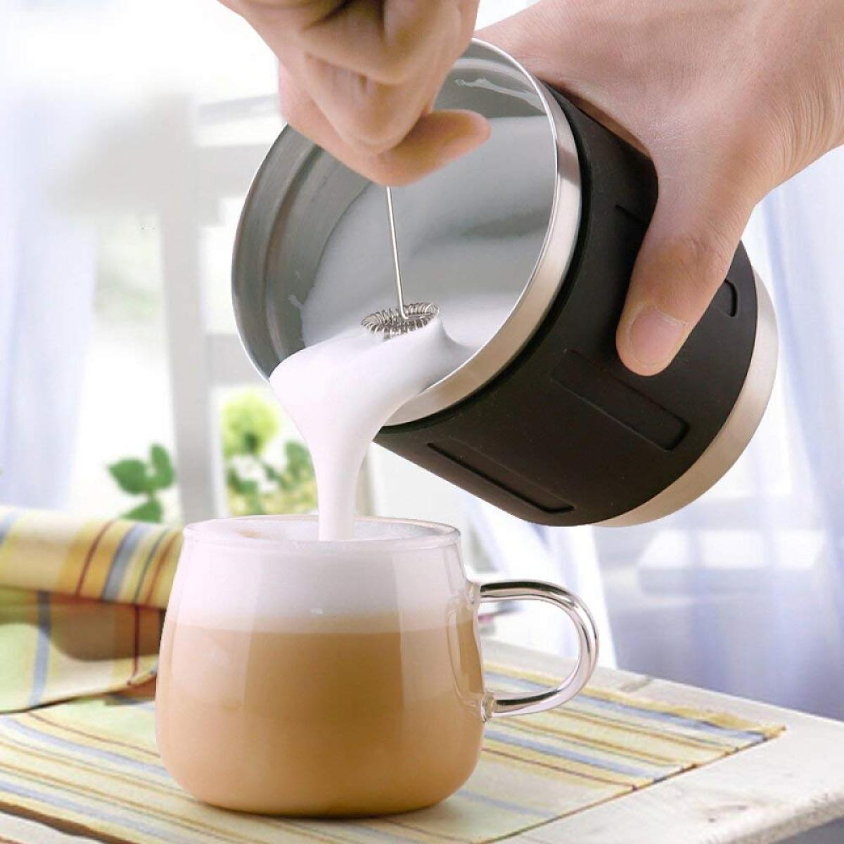 Hand schäumt Milch in eine klare Glas-Tasse mit Kaffee, wodurch ein Latte entsteht.